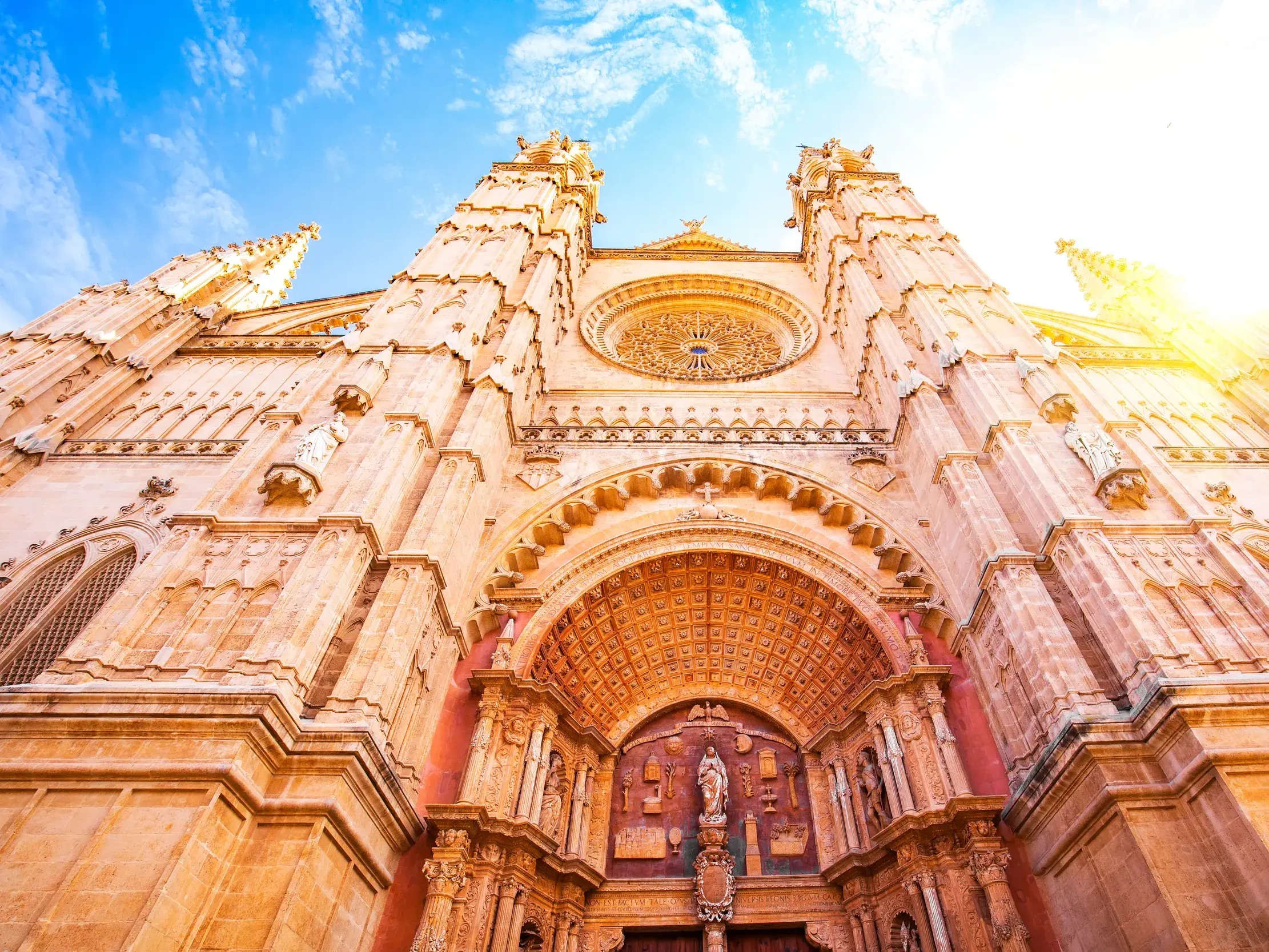 Die imposante gotische Fassade der Kathedrale von Palma de Mallorca ragt bei strahlendem Sonnenschein in den blauen Himmel.