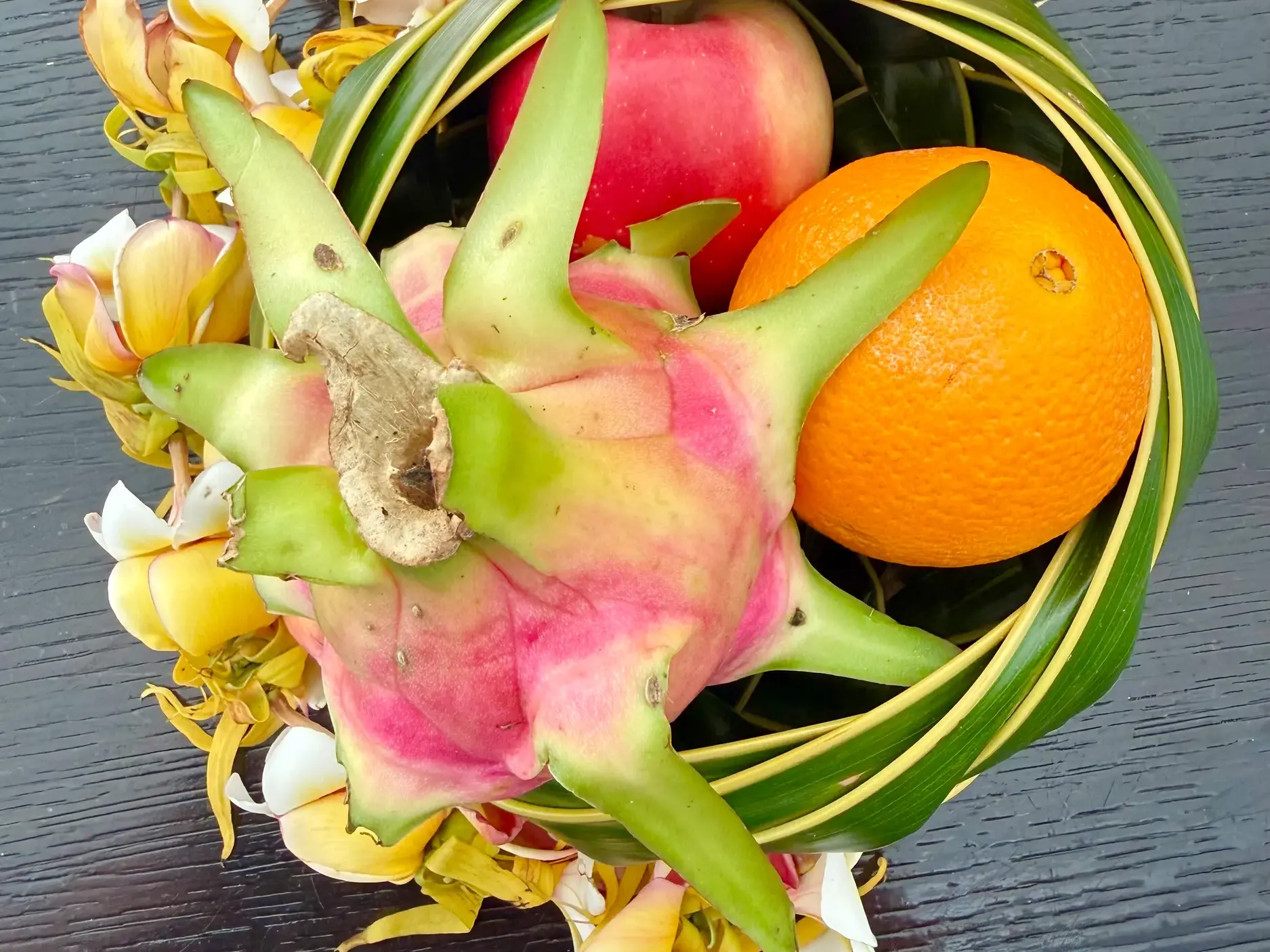 Ein aus Palmblättern geflochtener Korb mit einer Drachenfrucht, Orange und Blüten als Willkommensgruß auf Samoa.
