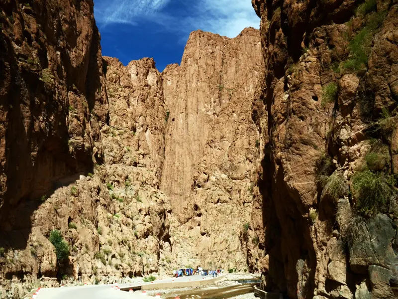 Imposante, steile Felswände der Todra-Schlucht in Marokko, in der eine kleine Reisegruppe auf der Straße wandert.