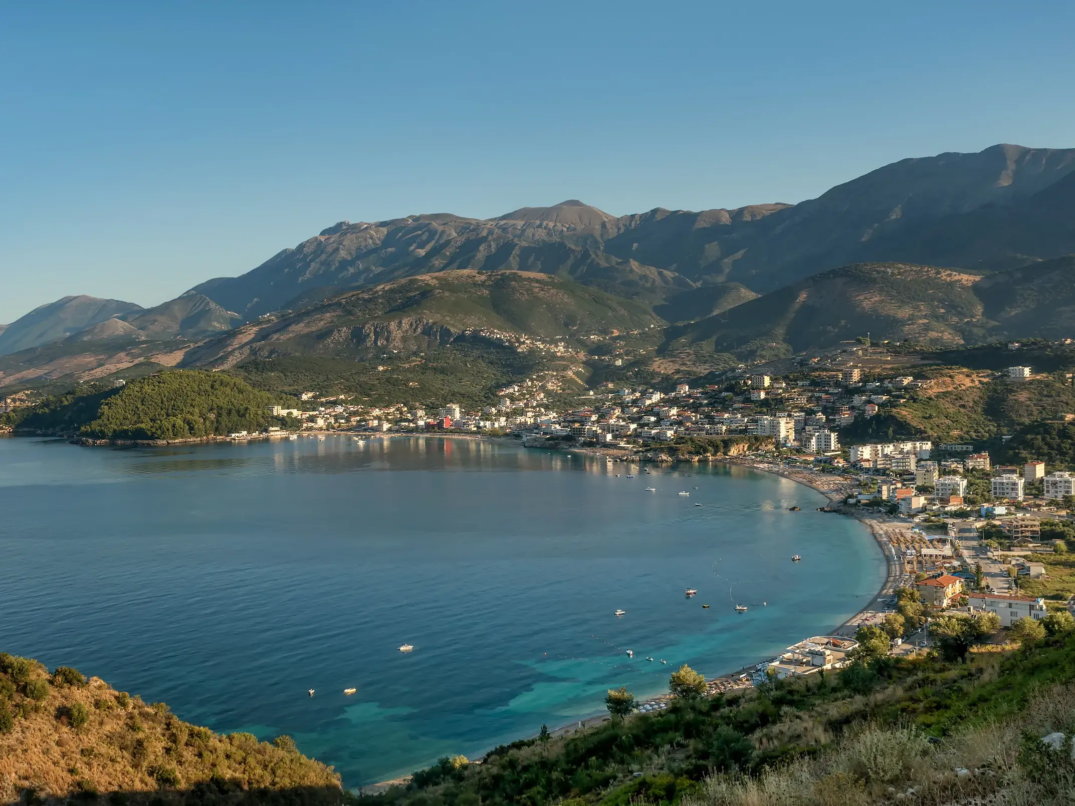 Sonnige Morgenstimmung über der Bucht von Himare an der albanischen Riviera, im Hintergrund das schroffe Küstengebirge.
