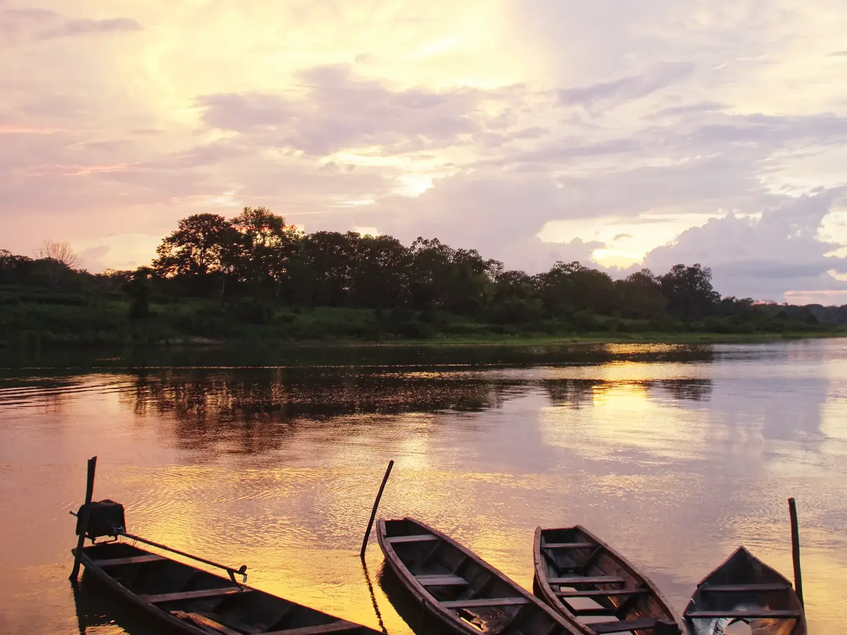 Am Ufer des Rio Don Diego in Kolumbien ruhen Boote im ruhigen Wasser, das den farbenprächtigen Sonnenuntergang spiegelt.