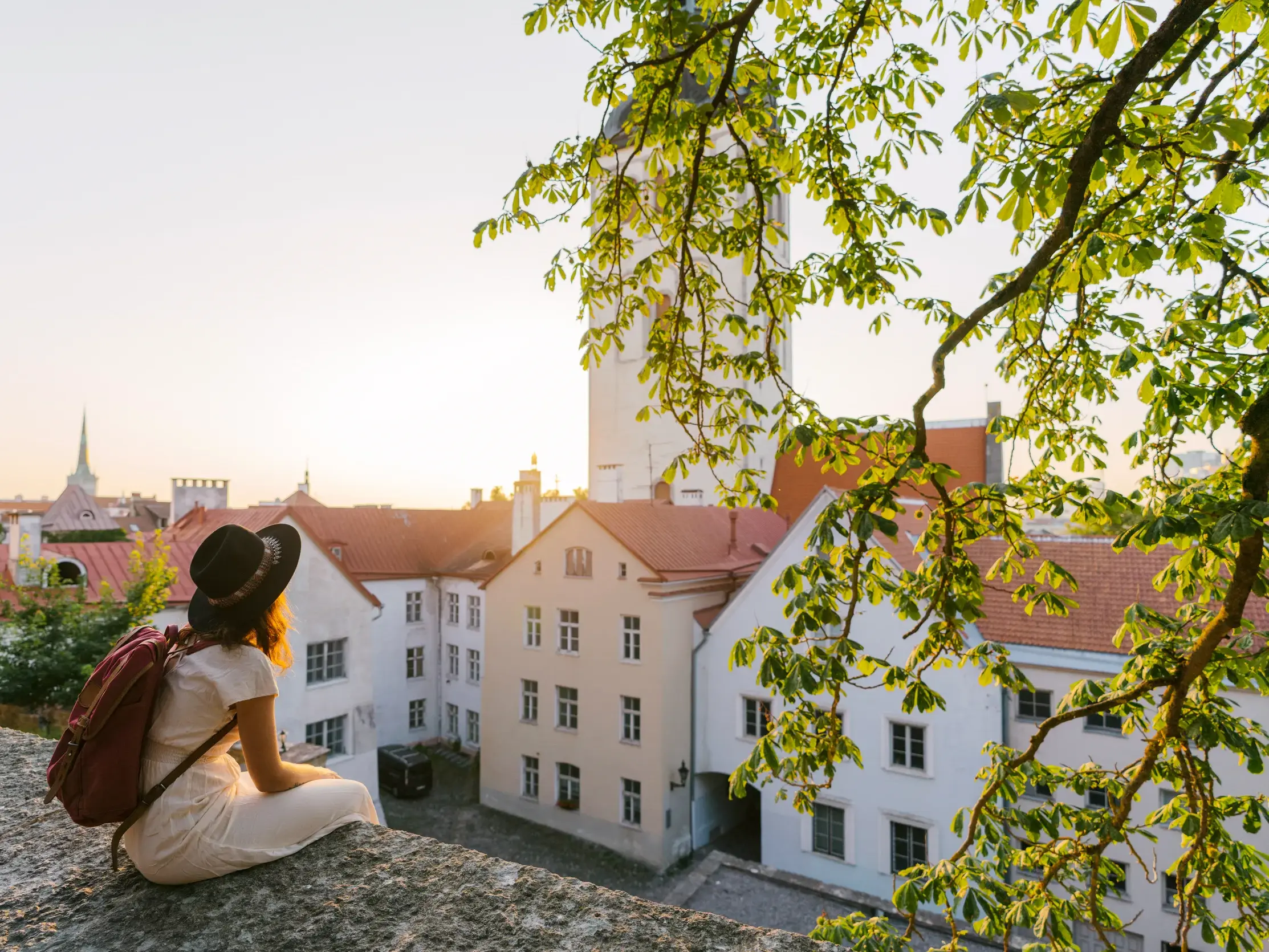 Eine Reisende mit Hut blickt vom Domberg über die Dächer der historischen Altstadt von Tallinn im Abendlicht.