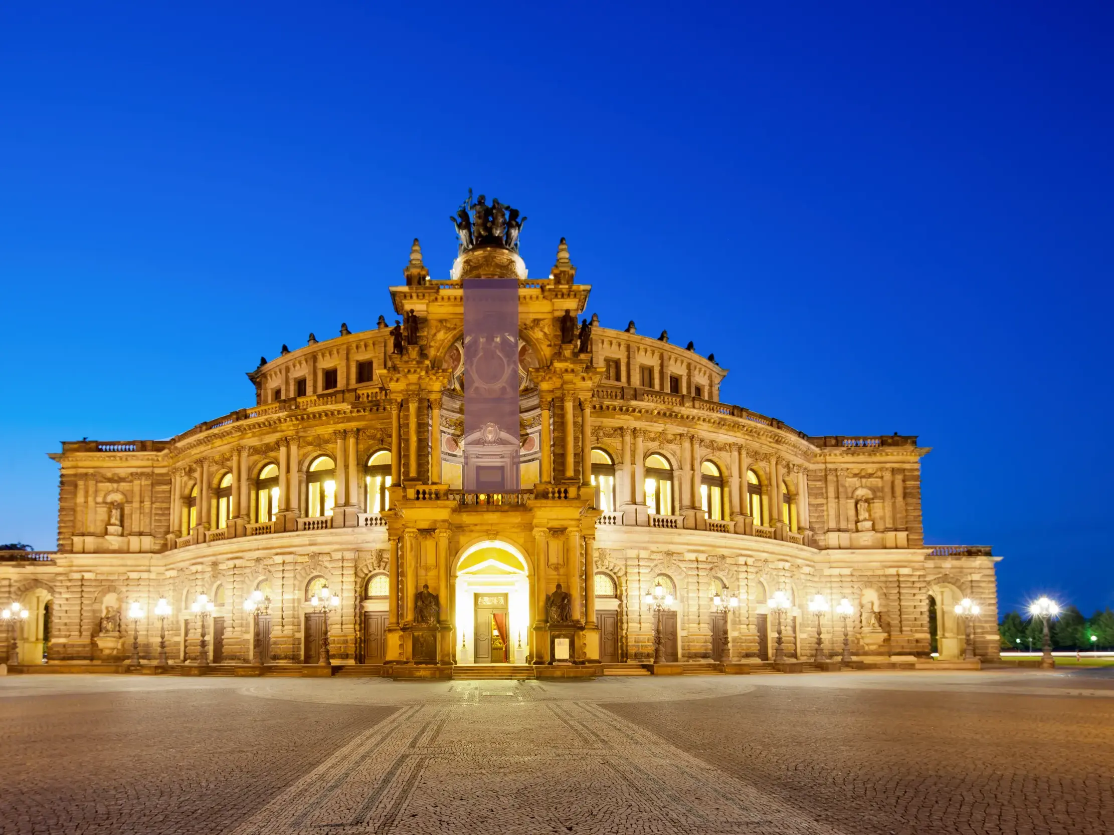 Die festlich beleuchtete Dresdner Semperoper am Theaterplatz in der Abenddämmerung.