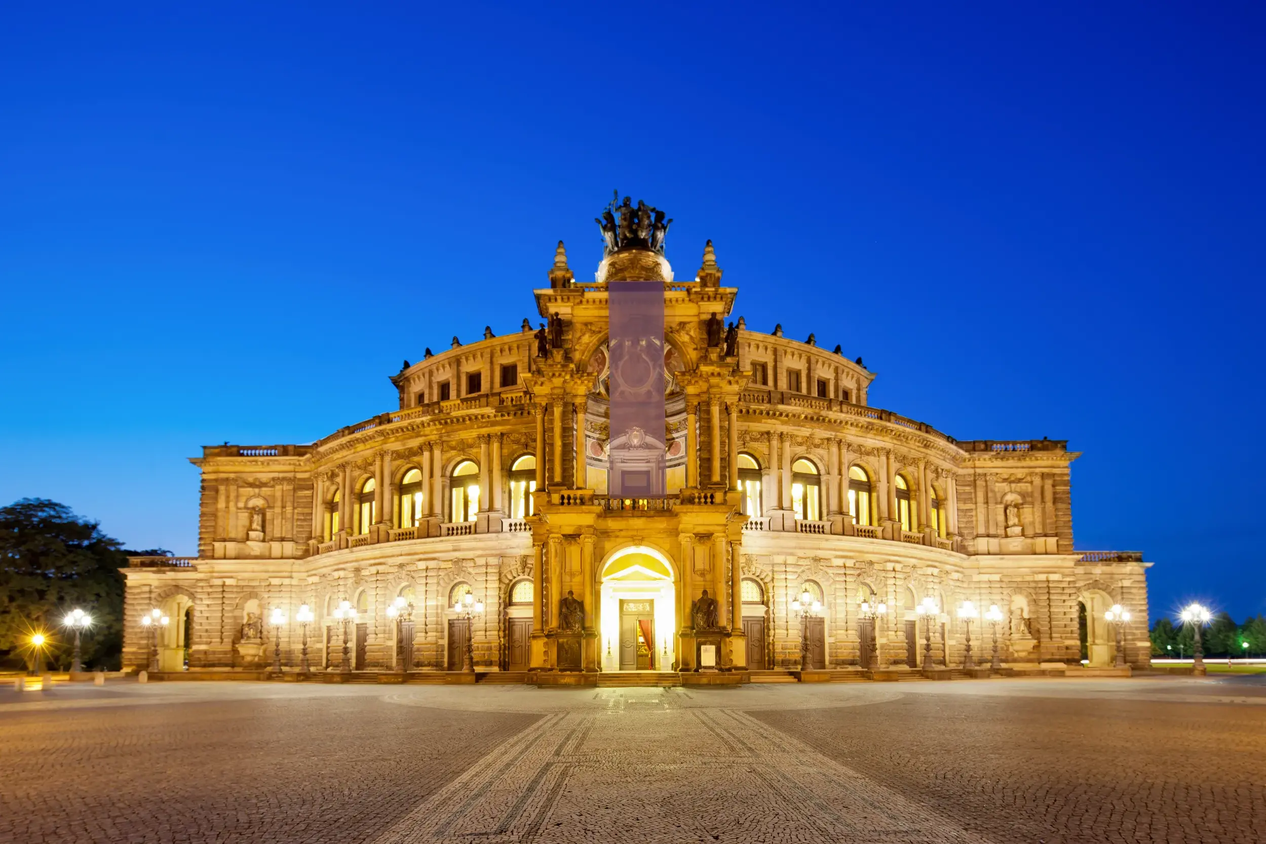 Die festlich beleuchtete Dresdner Semperoper am Theaterplatz in der Abenddämmerung.
