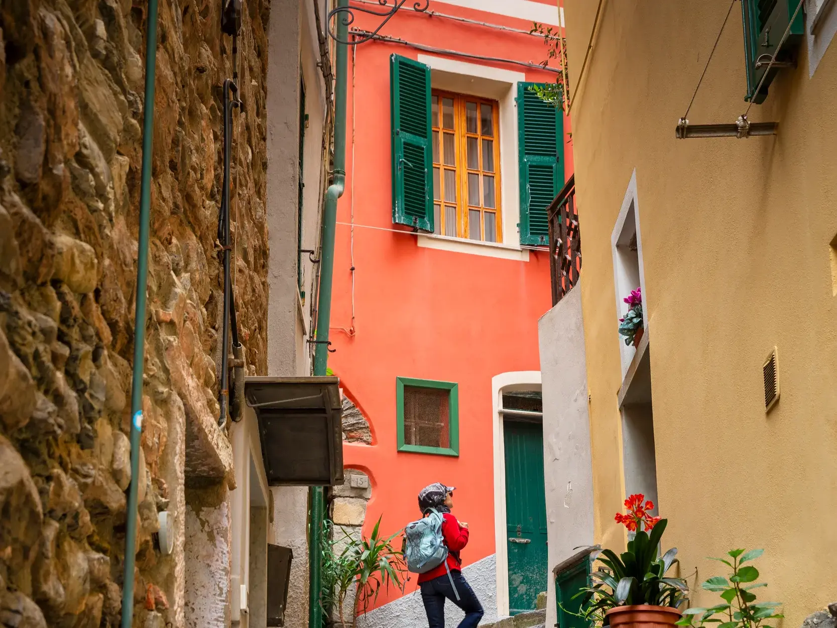 Eine Person mit Rucksack erkundet eine schmale Gasse zwischen farbenfrohen Häusern in einem Küstenort der Cinqueterre.