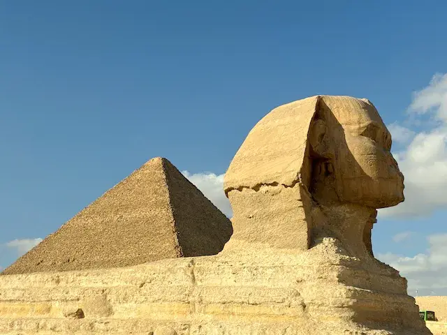 Der majestätische Große Sphinx von Gizeh im Profil, mit einer der berühmten Pyramiden im Hintergrund unter blauem Himmel.