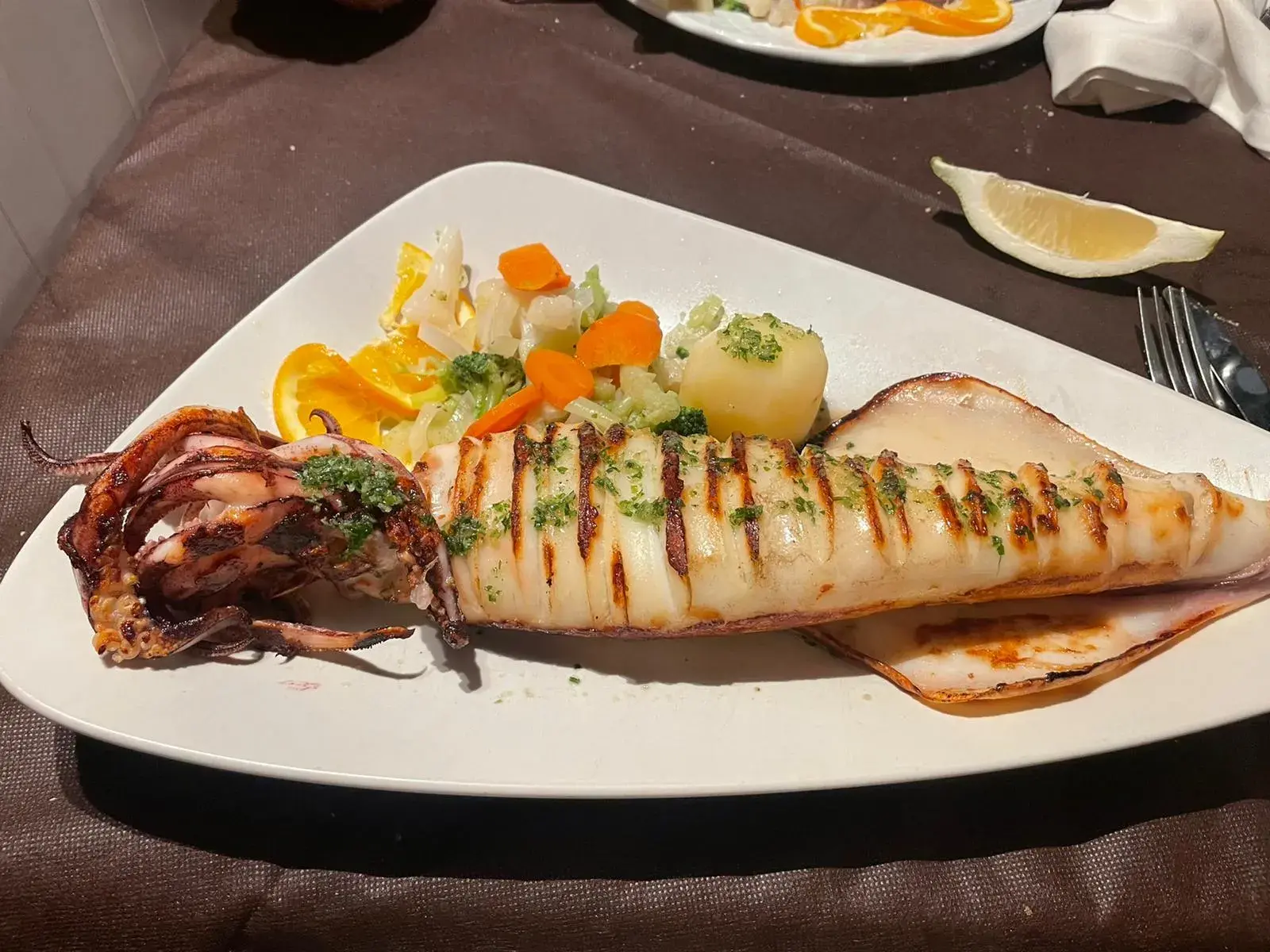 Zypriotische Meze: Ein ganzer gegrillter Tintenfisch mit Kräutern und Gemüse auf einem Teller in einer Taverne.