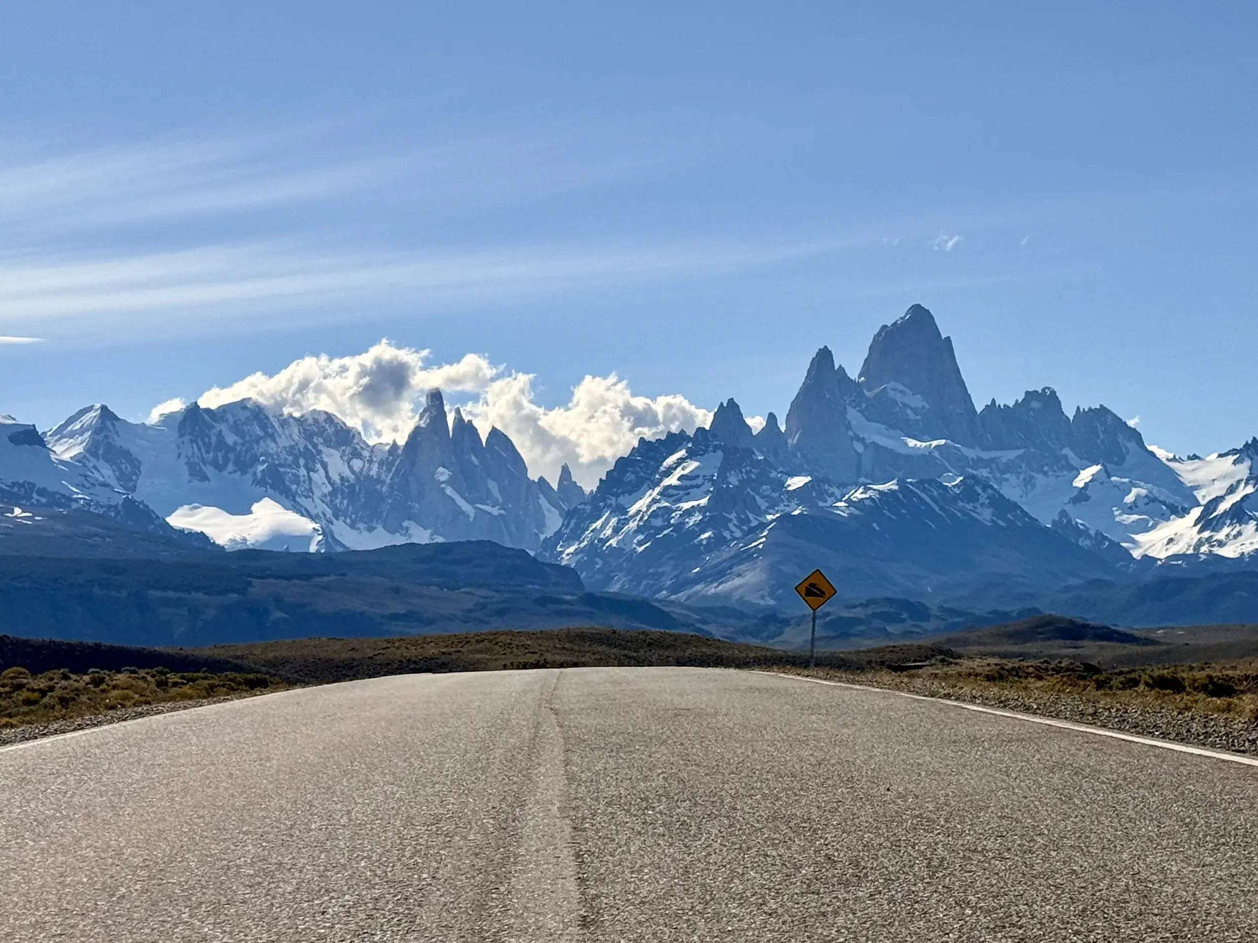 Eine leere Straße führt durch die patagonische Steppe auf das schneebedeckte Fitz Roy Massiv bei El Chaltén zu.