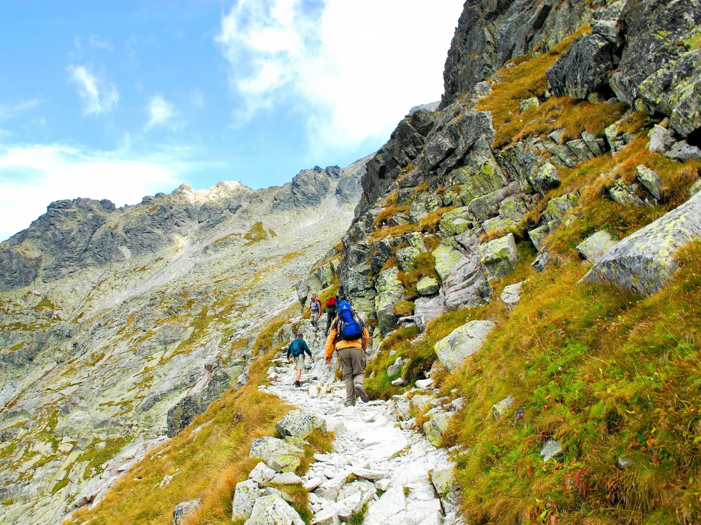 Eine kleine Wandergruppe mit Rucksäcken auf einem steinigen Bergpfad beim anspruchsvollen Aufstieg in der Hohen Tatra.