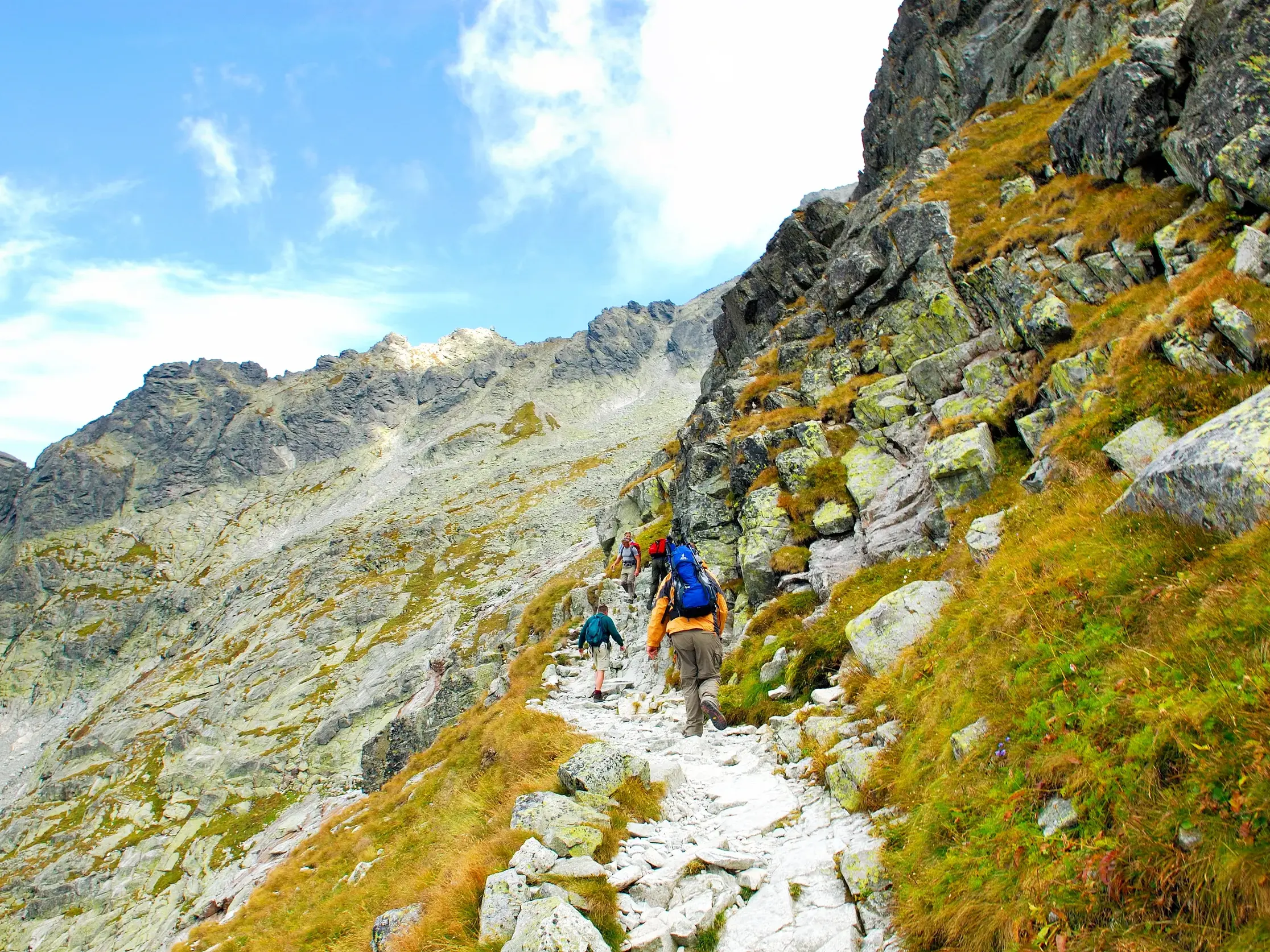 Eine Trekking-Gruppe auf einem schmalen Felsenpfad, der sich durch die steile Berglandschaft der Hohen Tatra schlängelt.
