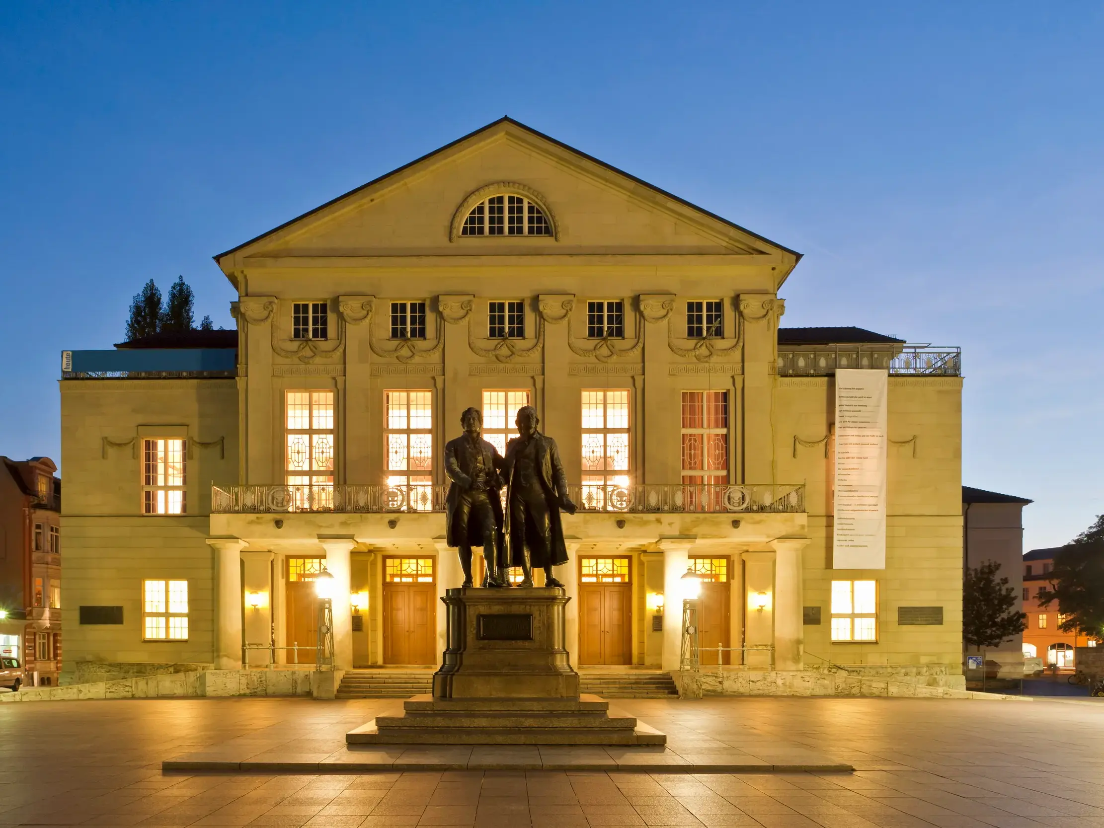 Das beleuchtete Nationaltheater in Weimar mit dem Goethe- und Schiller-Denkmal auf dem Theaterplatz am Abend