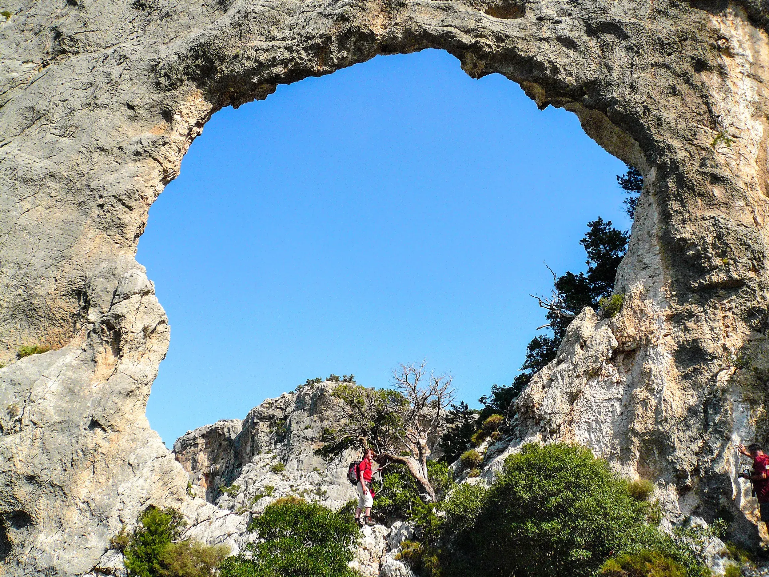 Majestätisches Felsentor auf dem Karsthochplateau Golgo auf Sardinien, ein Wanderer erkundet die Felslandschaft.
