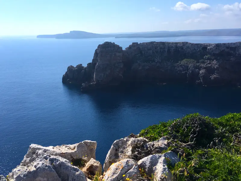 Wanderung auf dem Camí de Cavalls mit Ausblick von der Steilküste auf schroffe Felsen und das blaue Meer Menorcas.