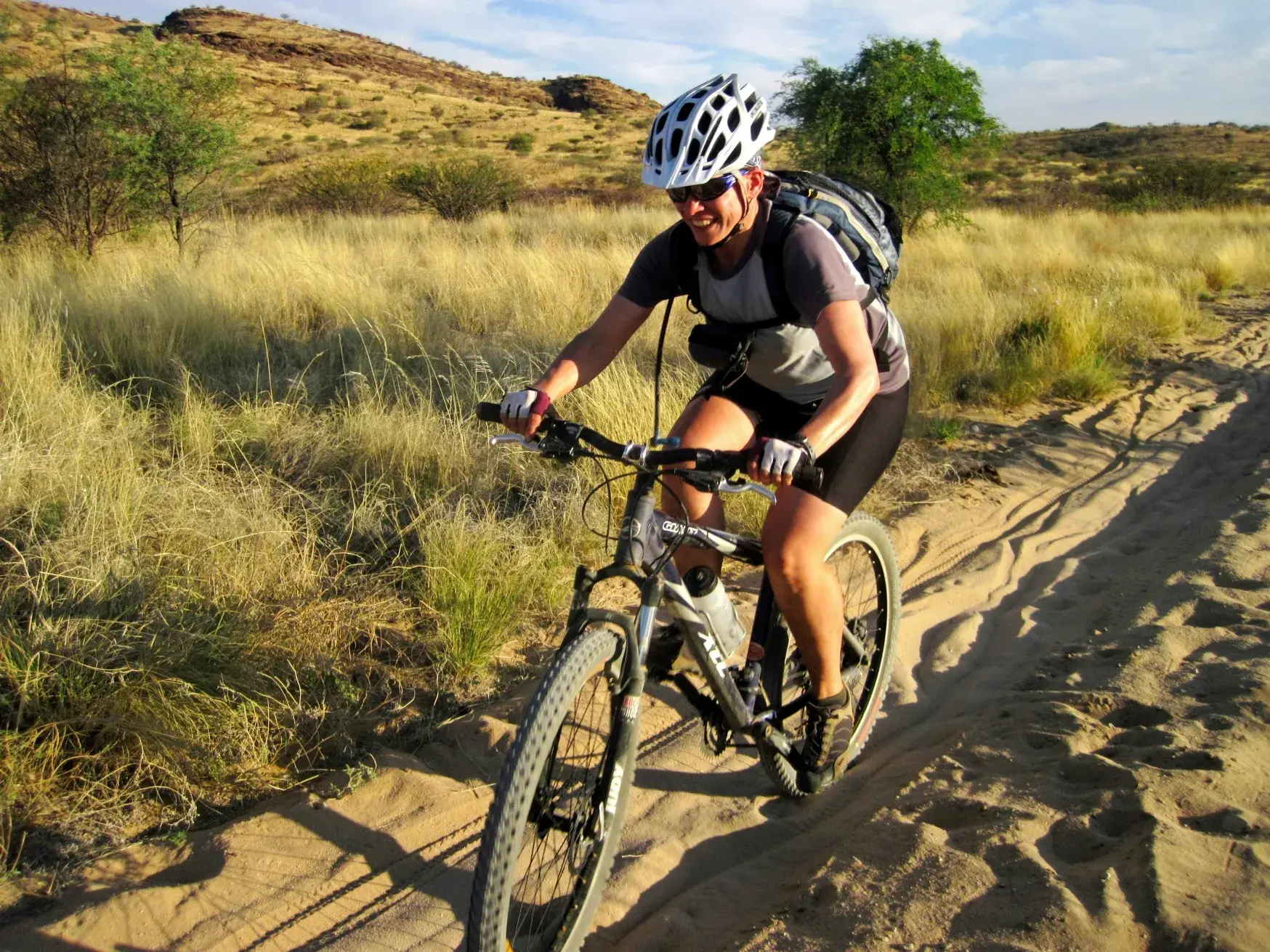 Eine Mountainbikerin fährt mit Helm und Rucksack auf einem tiefen Sandweg durch die trockene Savanne Namibias.