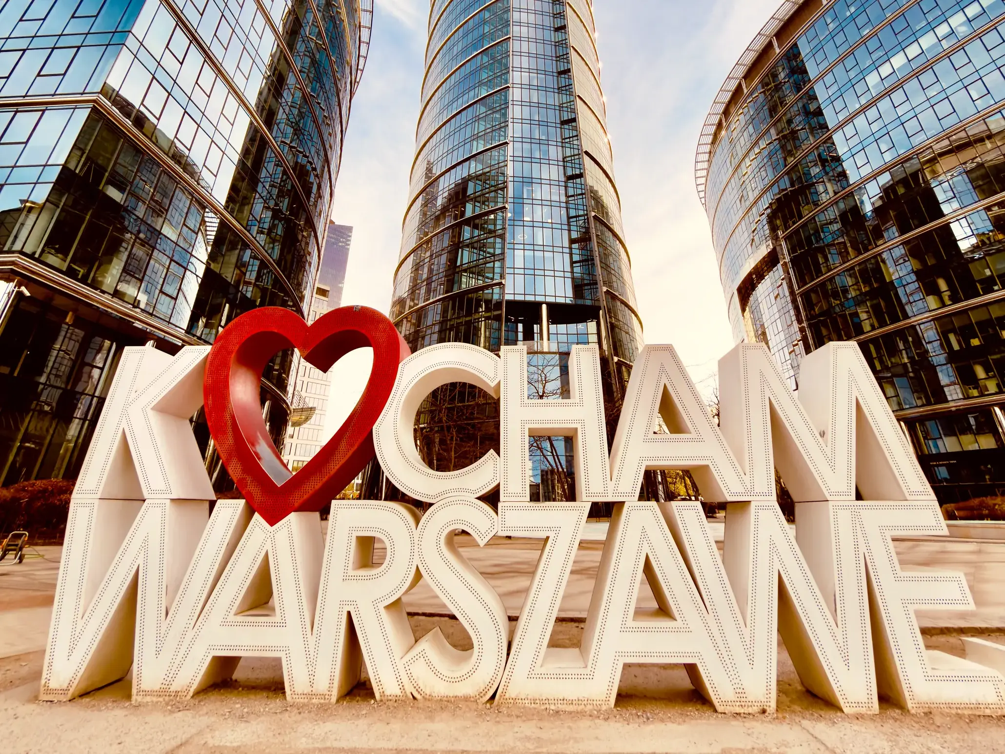 Der "Kocham Warszawę"-Schriftzug, ein beliebtes Fotomotiv, vor der modernen Skyline aus Glas und Stahl in Warschau.