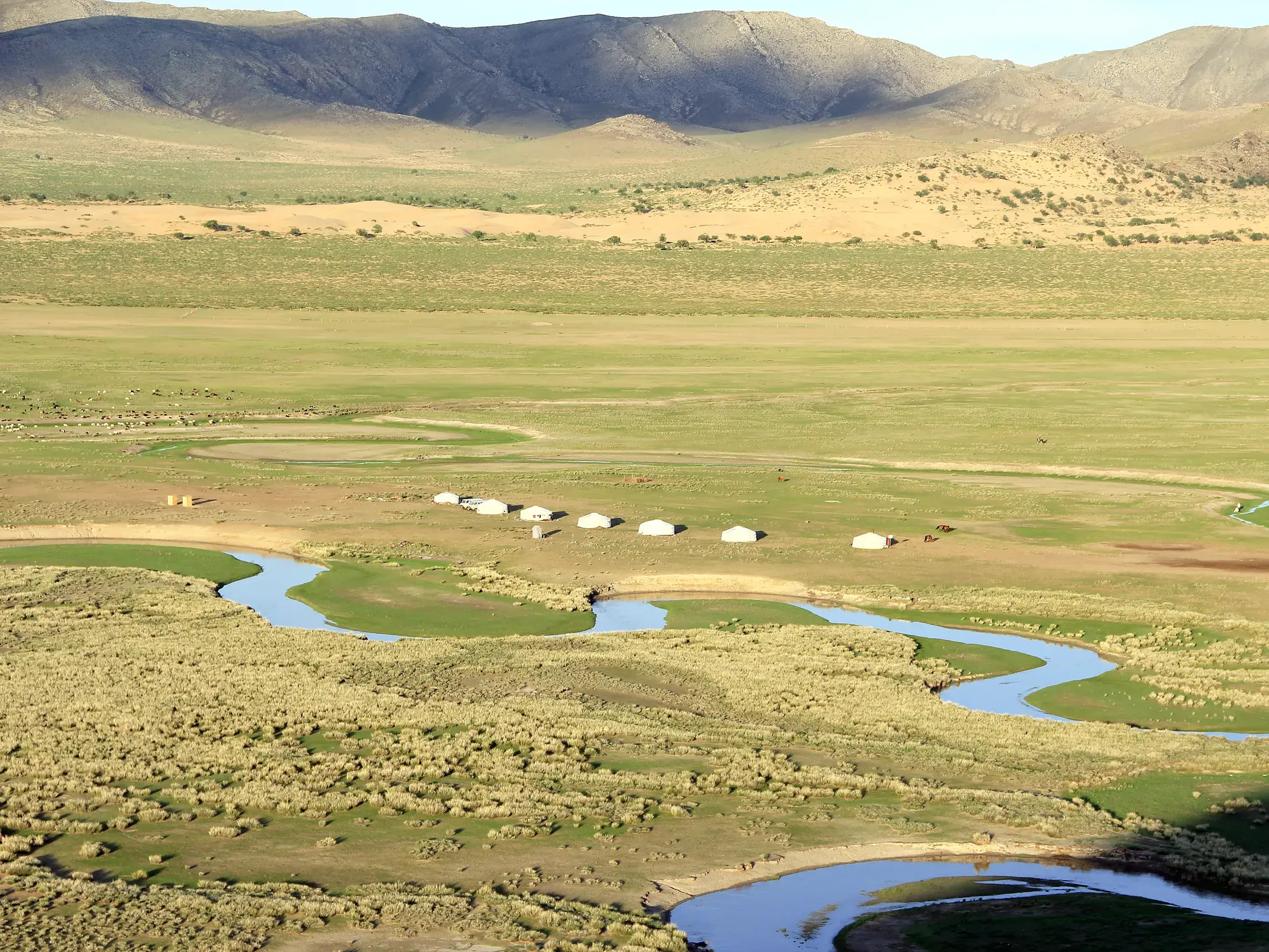 Authentisches Jurtenlager für eine Wanderreise am Ufer eines Flusses in der unendlichen Weite der mongolischen Steppe.