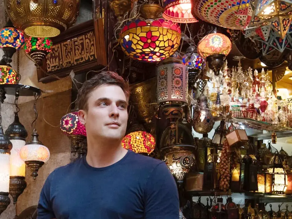 Autor Constantin Schreiber umgeben von kunstvollen orientalischen Glasmosaik-Lampen in einem Basar in Kairo