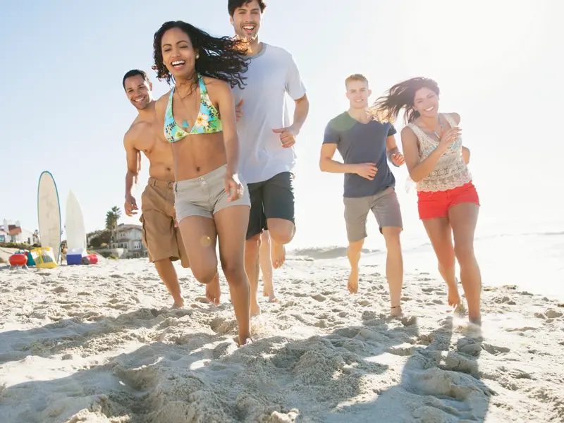 Eine fröhliche junge Reisegruppe rennt bei strahlendem Sonnenschein über einen Sandstrand in der Dominikanischen Republik.