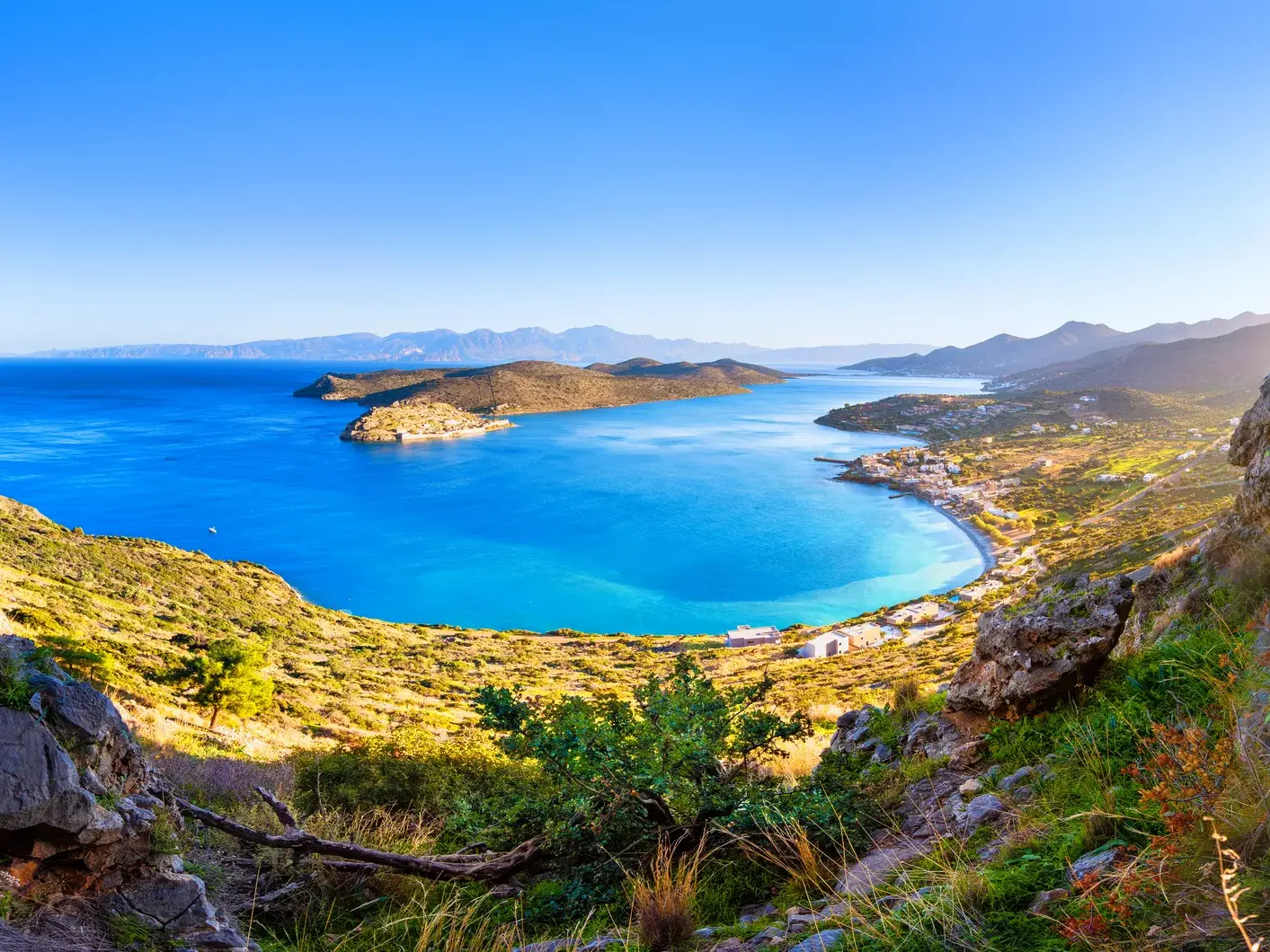 Panoramablick von den Küstenbergen auf das tiefblaue Meer, die Insel Spinalonga und den Küstenort Elounda auf Kreta.