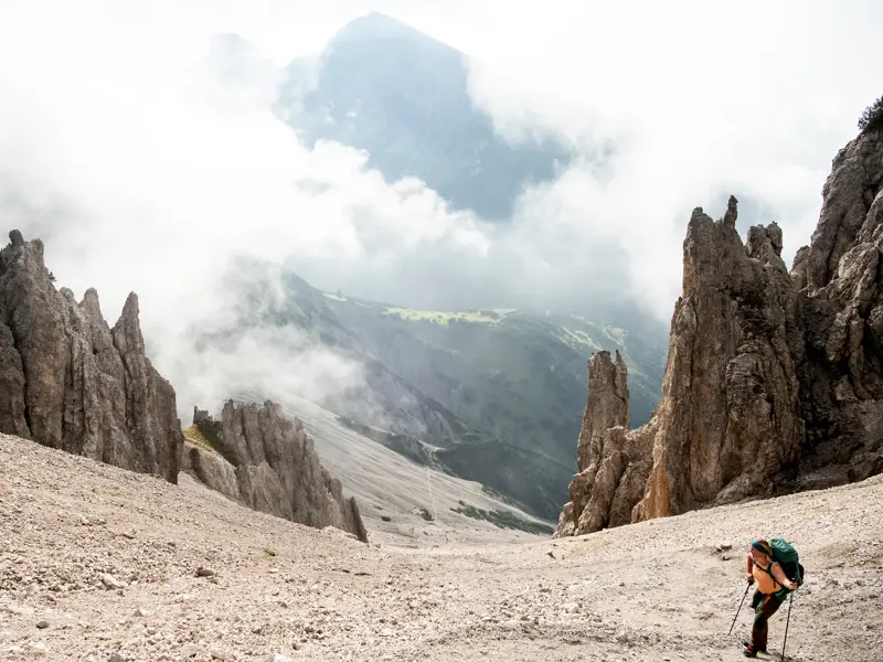 Frau mit Trekking-Rucksack wandert durch ein Geröllfeld mit Felsnadeln auf dem Weg zur Eppzirler Scharte im Karwendelgebirge.