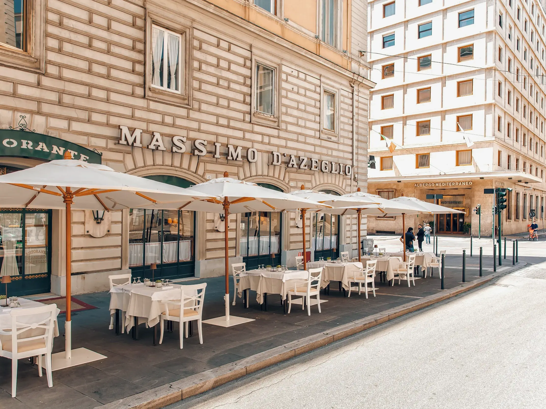 Sonnige Außenansicht des Hotel Massimo d'Azeglio in Rom mit der Terrasse des Ristorante und weiß gedeckten Tischen.