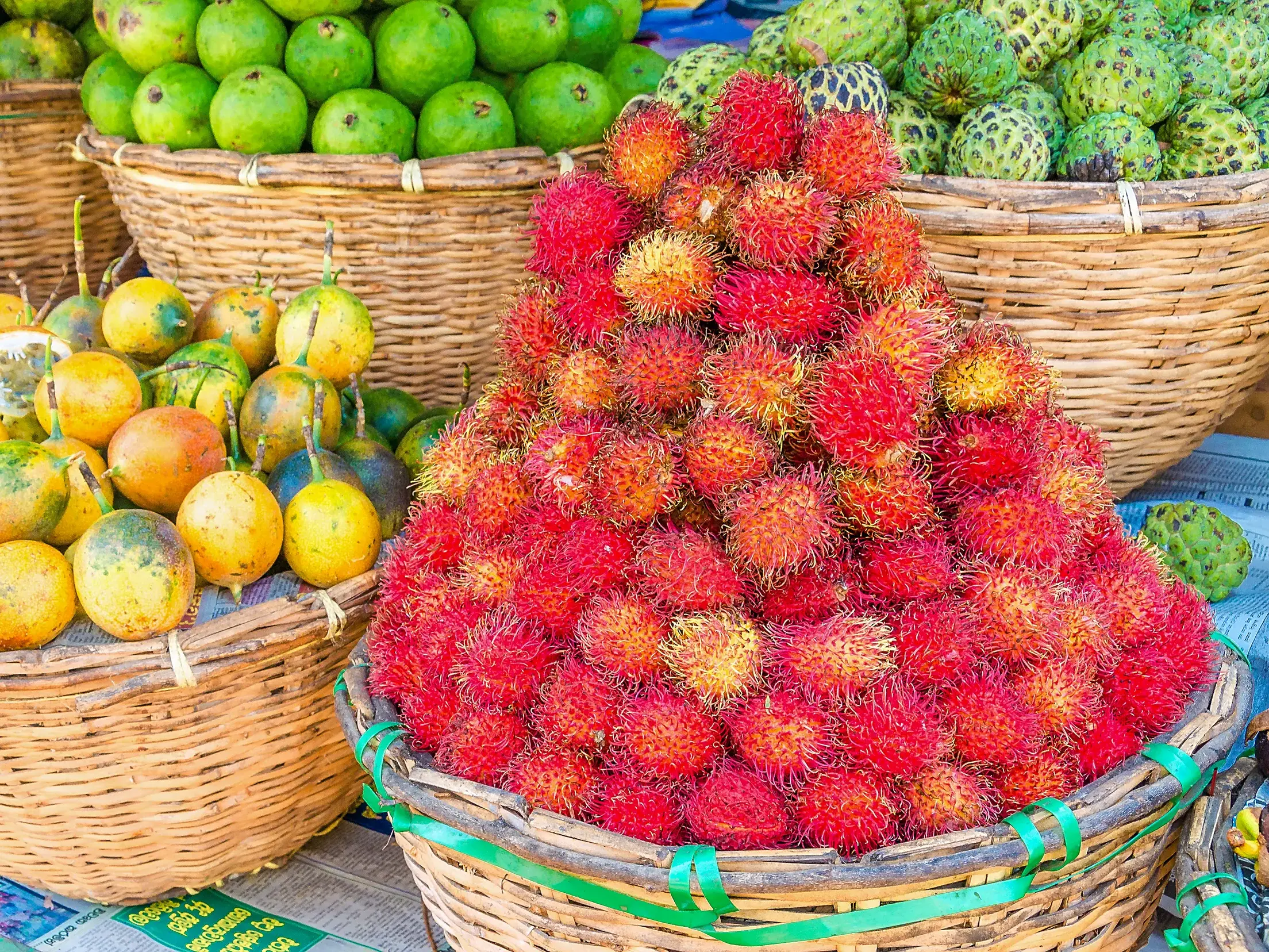 Körbe mit frischen, exotischen Früchten wie Rambutan und Passionsfrucht auf dem bunten Dambulla-Markt in Sri Lanka.