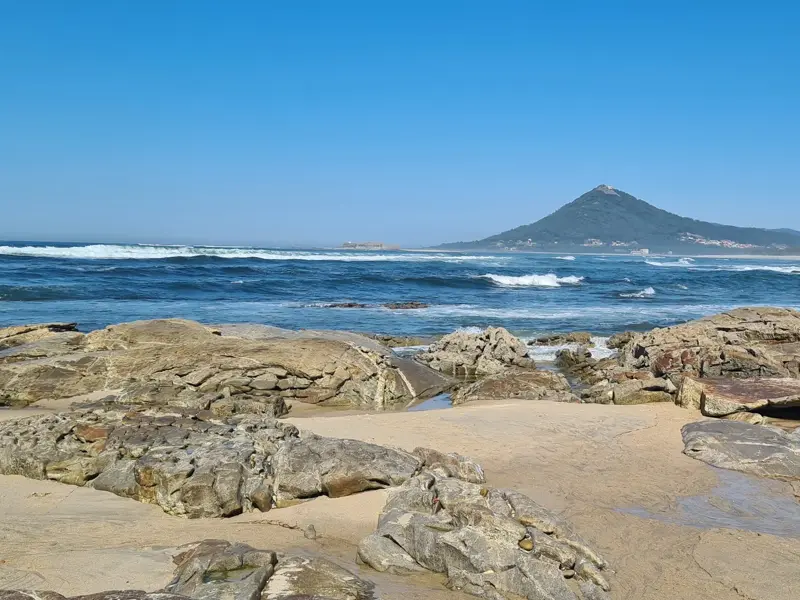 Küstenwanderung am Jakobsweg in Portugal: felsiger Strand mit Blick auf den Monte de Santa Luzia bei Vila Praia de Ancora.