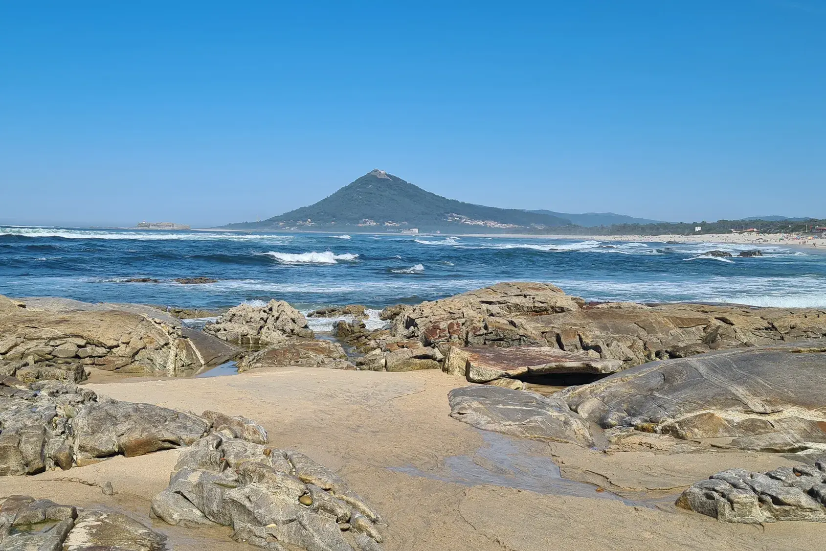Küstenwanderung am Jakobsweg: Felsen am Sandstrand bei Caminha mit Blick über den Atlantik auf die Basilika Santa Luzia.