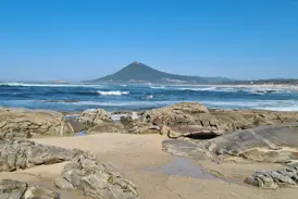 Küstenwanderung am Jakobsweg: Felsen am Sandstrand bei Caminha mit Blick über den Atlantik auf die Basilika Santa Luzia.