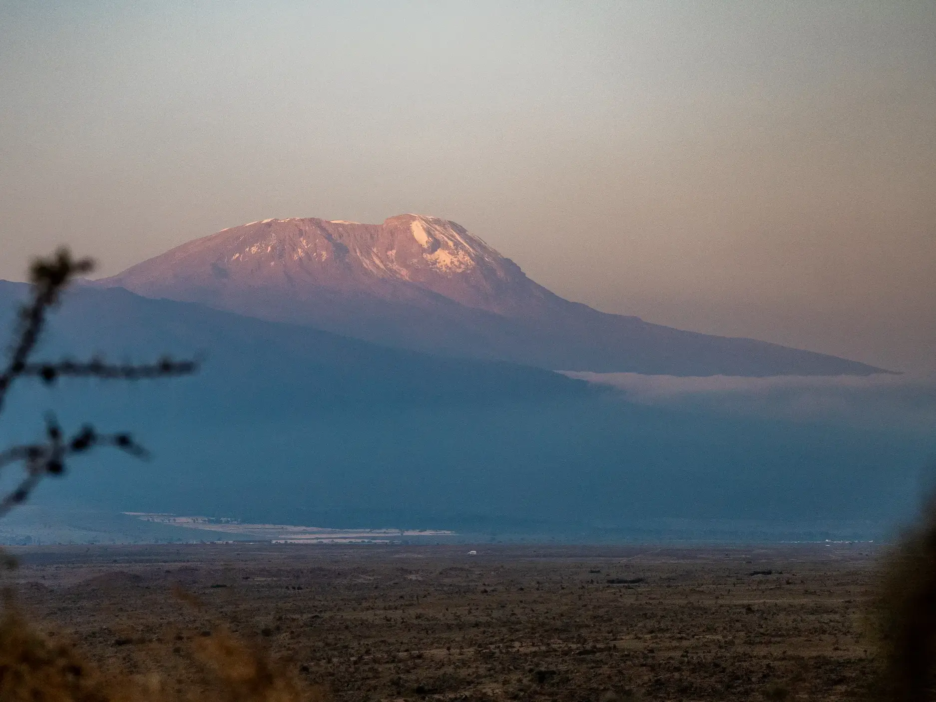 Der schneebedeckte Gipfel des Kilimanjaro im Morgenlicht, gesehen über die weite, trockene Massai-Steppe in Tansania.