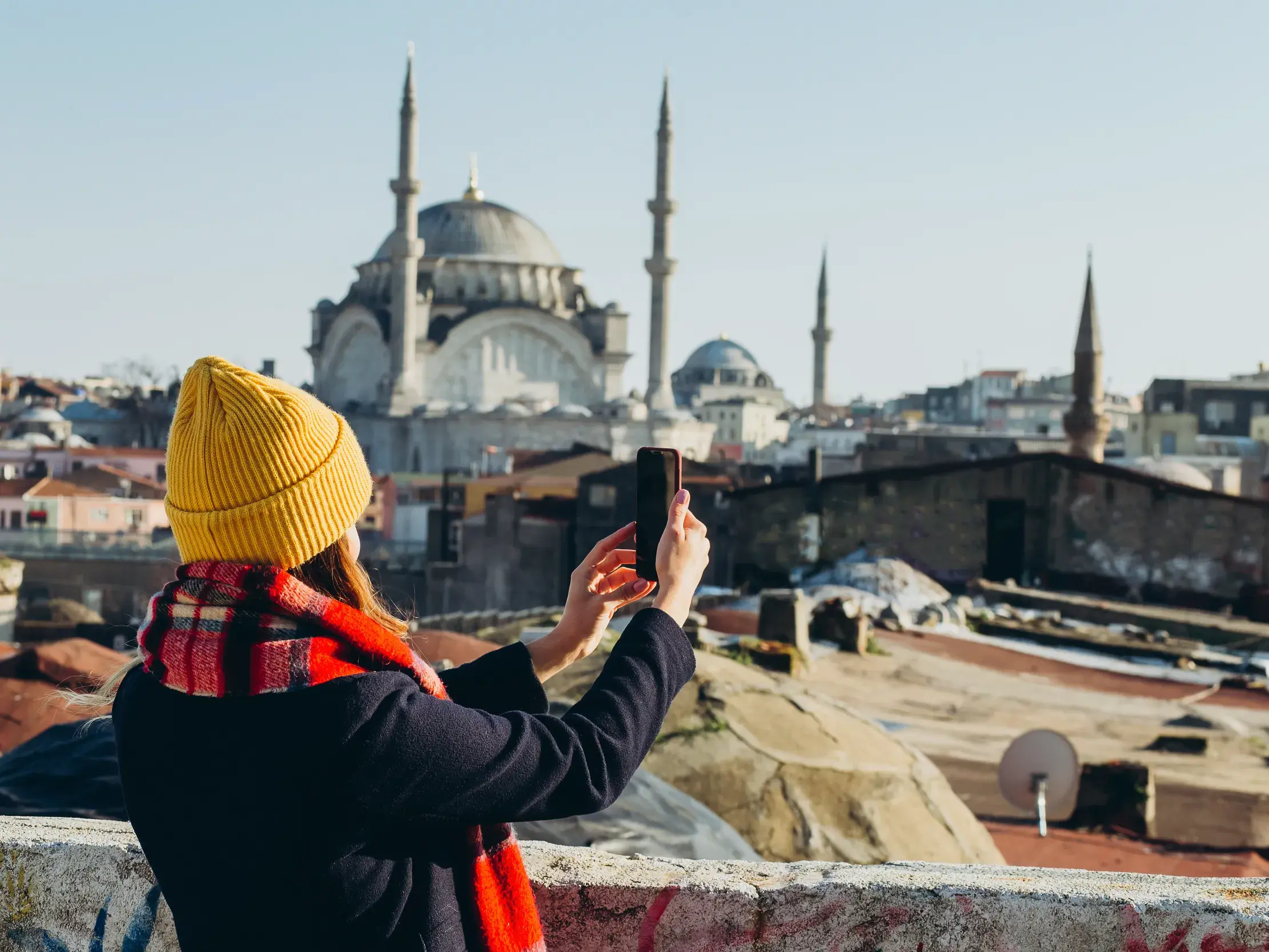 Eine Frau mit gelber Mütze fotografiert mit ihrem Smartphone die Süleymaniye-Moschee über den Dächern von Istanbul.
