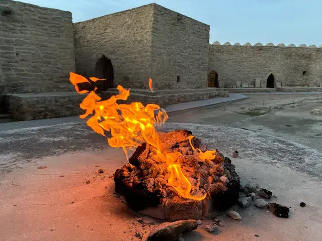 Die ewige Flamme des Feuertempels Ateschgah in Baku lodert in einer Feuerstelle vor den historischen Steinmauern.