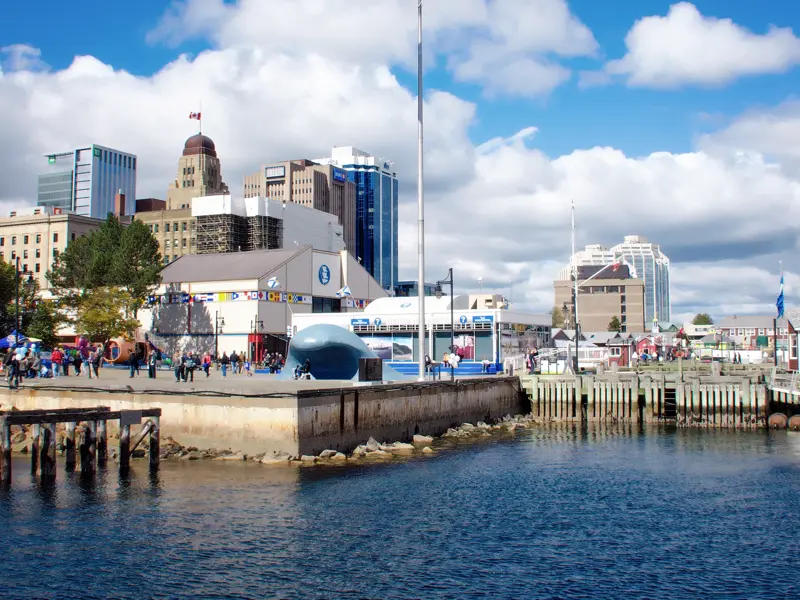 Die belebte Uferpromenade von Halifax in Nova Scotia mit Spaziergängern und der Skyline der Stadt unter blauem Himmel.