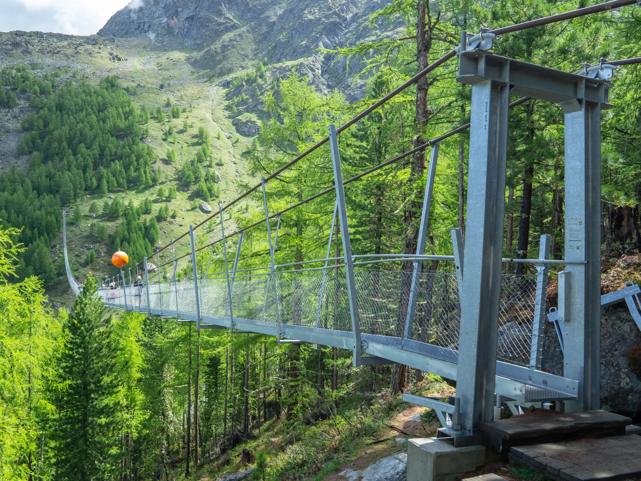Wanderer überqueren die lange Charles Kuonen Hängebrücke, die sich auf dem Europaweg über ein tiefes, bewaldetes Tal spannt.