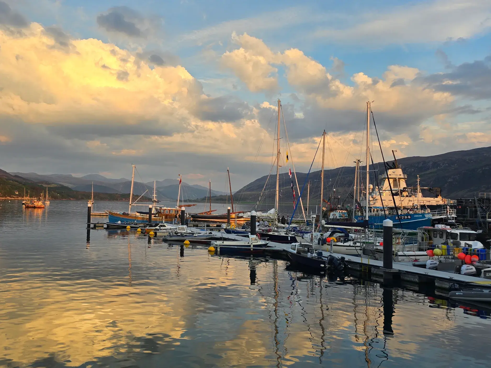 Segelboote und Fischerboote im Hafen von Ullapool am Loch Broom bei Sonnenuntergang in den North West Highlands.