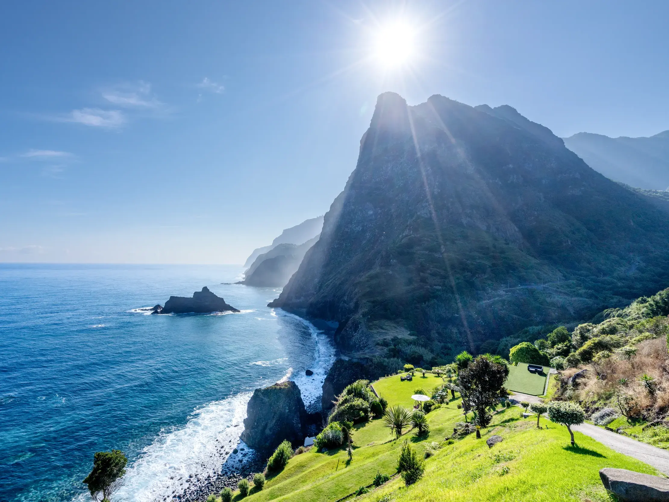 Dramatische Vulkanlandschaft an Madeiras Steilküste, die bei strahlendem Sonnenschein in den tiefblauen Atlantik ragt.