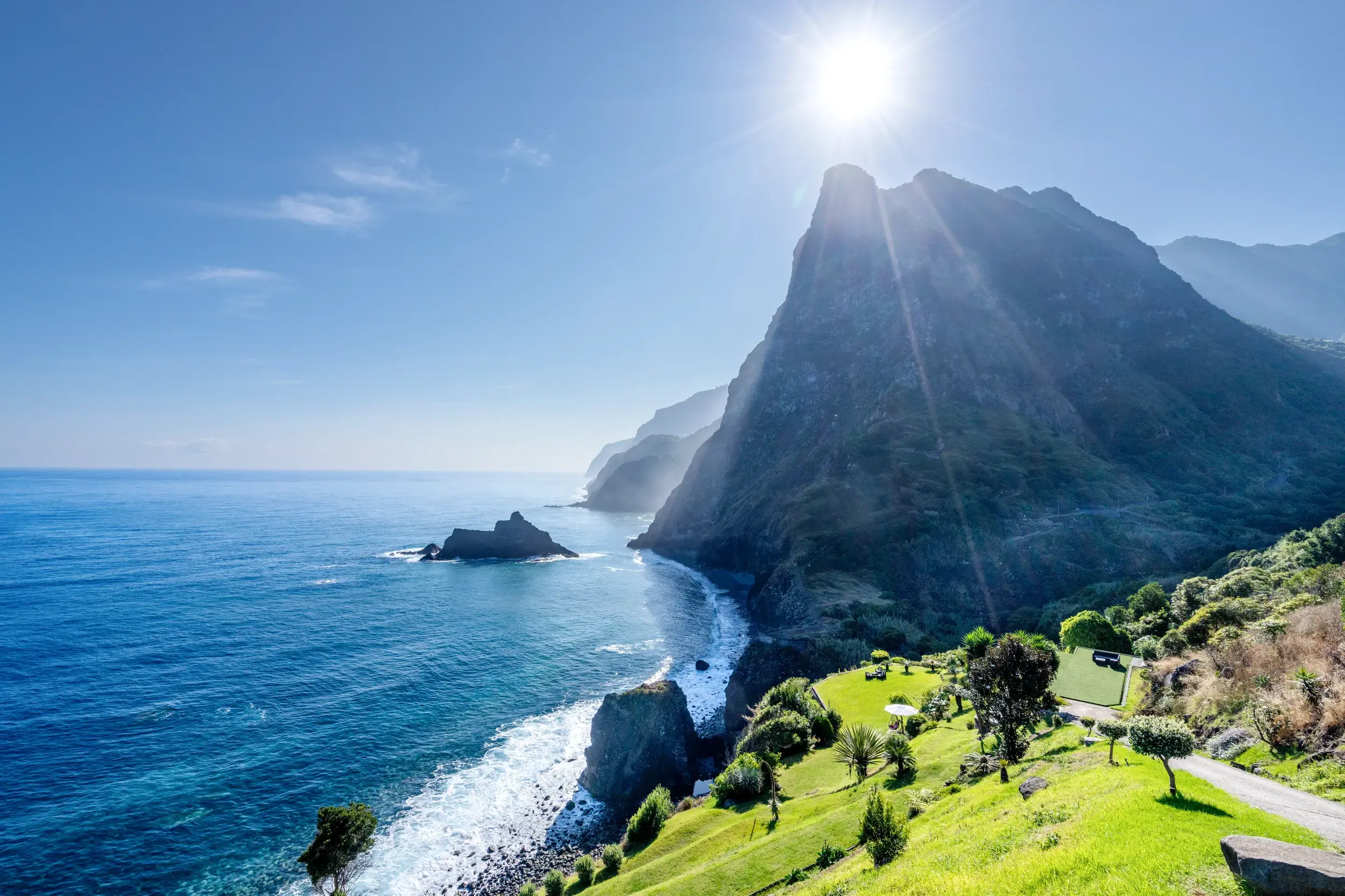 Dramatische Vulkanlandschaft an Madeiras Steilküste, die bei strahlendem Sonnenschein in den tiefblauen Atlantik ragt.