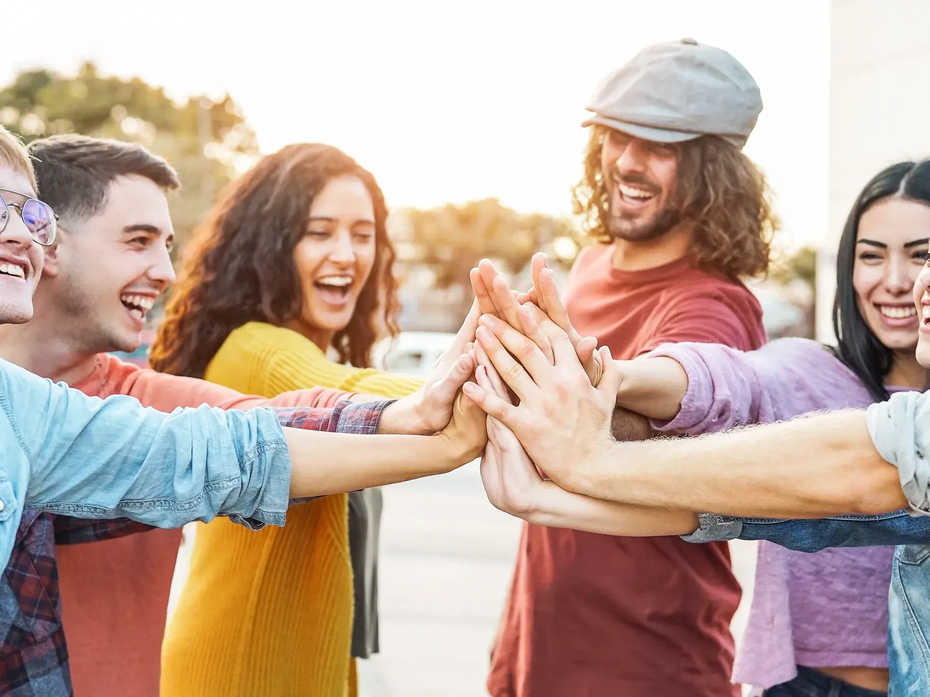 Eine Gruppe junger Leute auf einer Gruppenreise legt draußen lachend ihre Hände zu einem gemeinsamen High-Five zusammen.