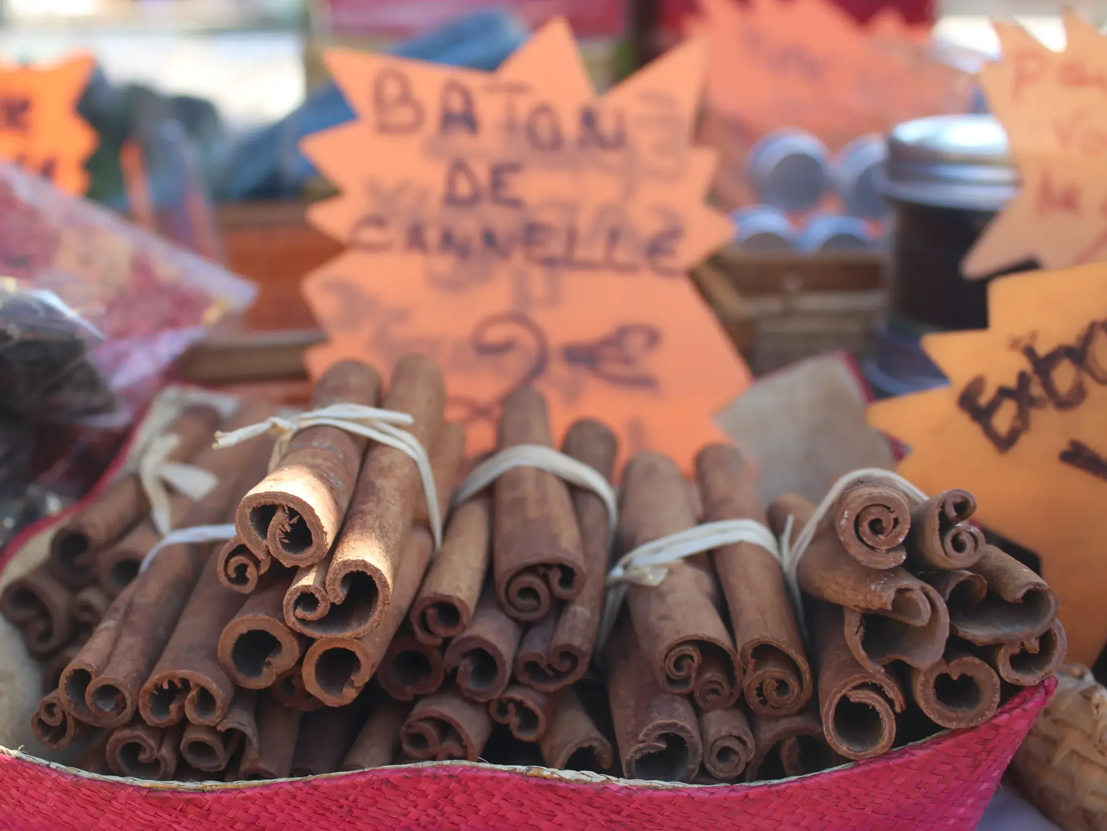 Gebündelte Zimtstangen in einem roten Korb auf einem Marktstand in Saint-Pierre, La Réunion, mit weiteren lokalen Gewürzen.