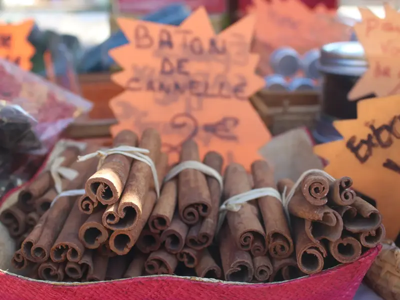 Gebündelte Zimtstangen in einem roten Korb auf einem Marktstand in Saint-Pierre, La Réunion, mit weiteren lokalen Gewürzen.