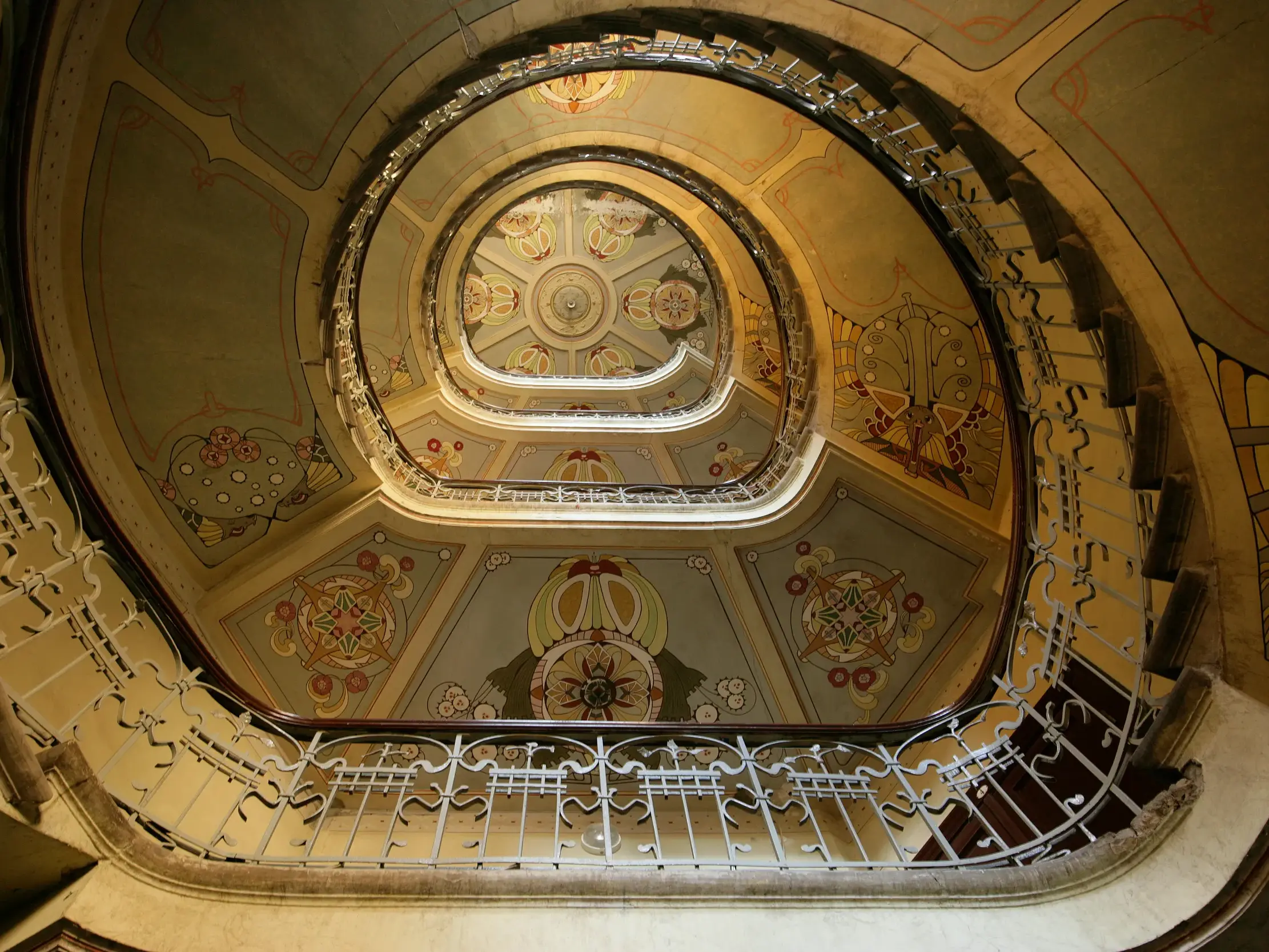 Aufwärtsblick durch ein prunkvolles, spiralförmiges Treppenhaus mit Deckenmalereien im Jugendstilviertel von Riga.