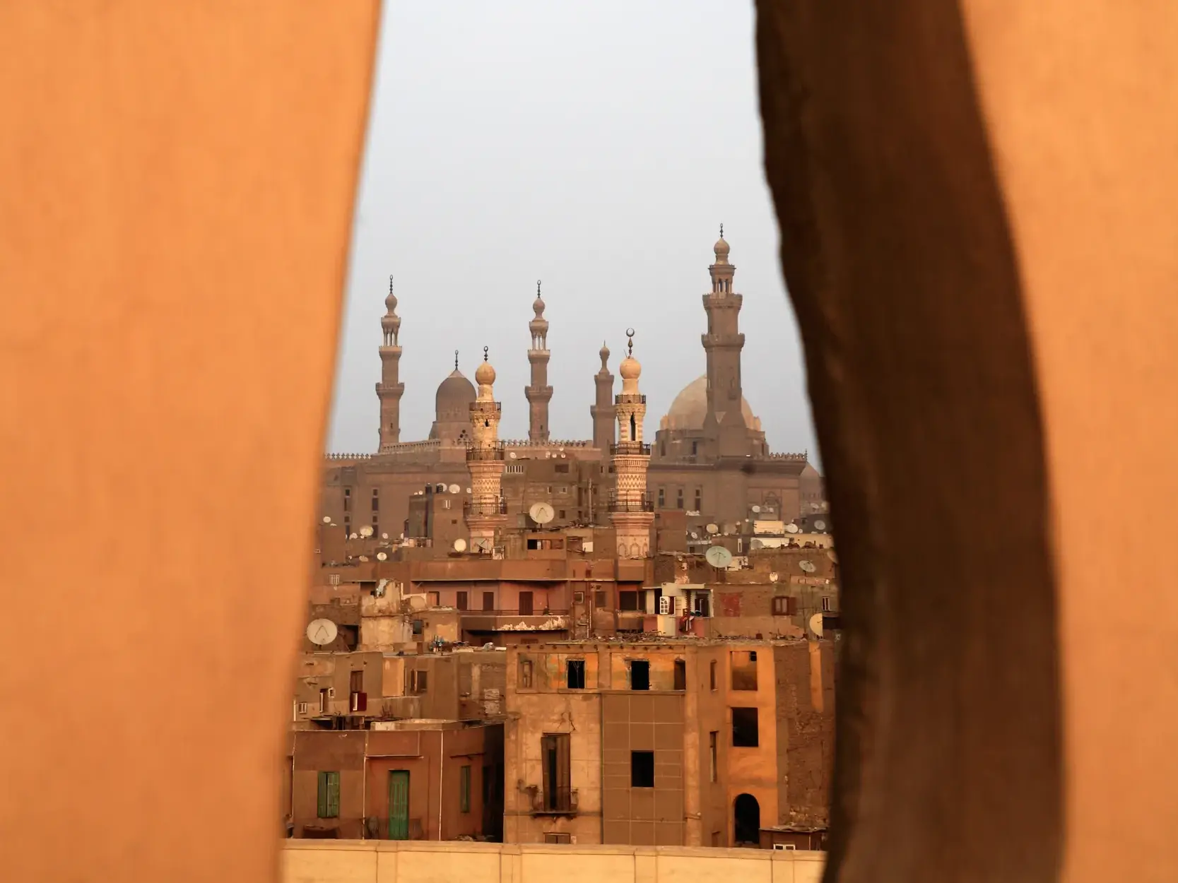 Ausblick von einem Minarett über die dicht bebauten Dächer und Moscheen der historischen Altstadt von Kairo bei diesigem Himmel.