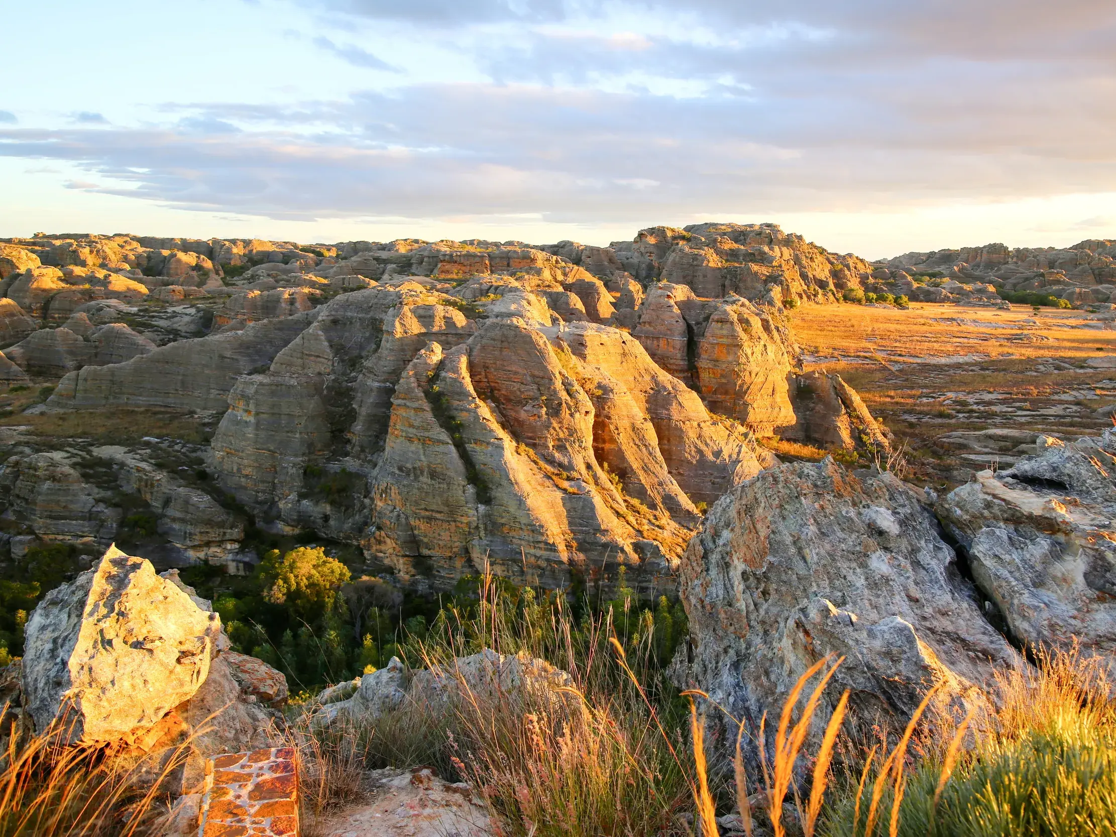 Weitläufige Landschaft mit bizarren Sandsteinformationen im Isalo-Nationalpark, die von der Abendsonne beleuchtet werden.