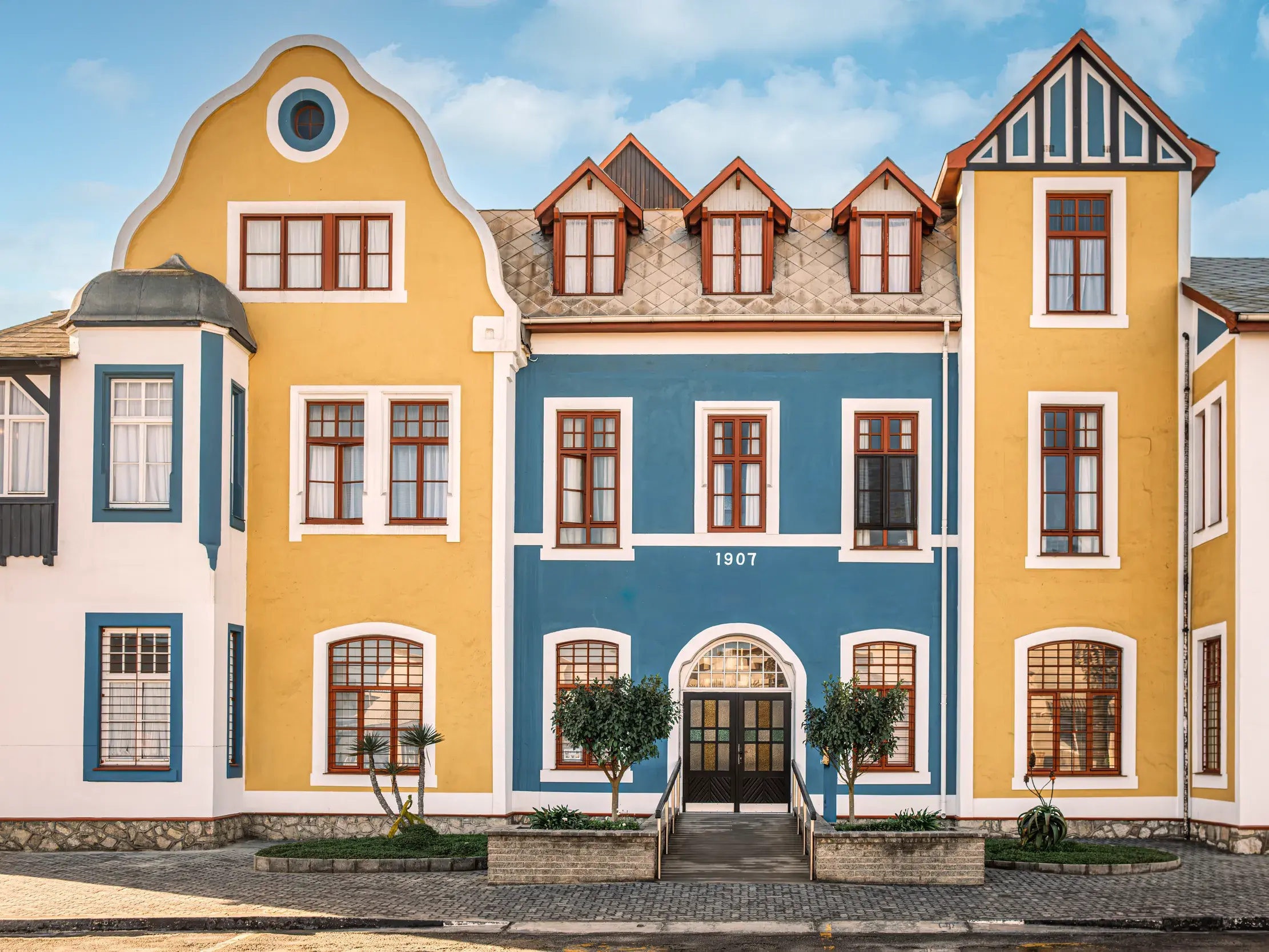 Prachtvolle, gelb-blaue Fassade eines historischen Gebäudes im wilhelminischen Kolonialstil in Swakopmund erleben Reisegäste bei der Rundreise, mit Studiosus in Namibia.