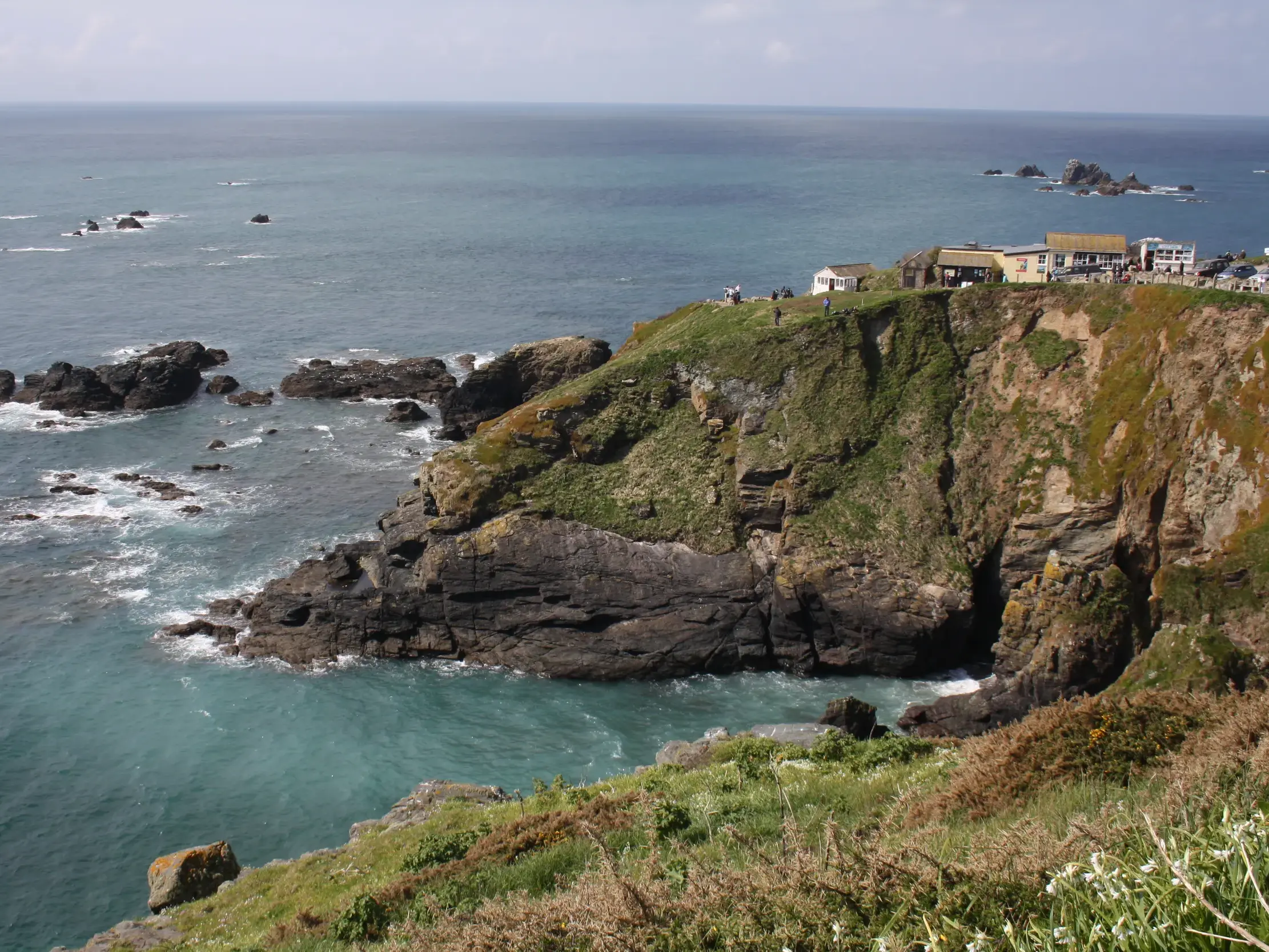 Schroffe, grasbewachsene Klippen von Land's End in Cornwall, wo Wanderer den weiten Blick über den Atlantik genießen.