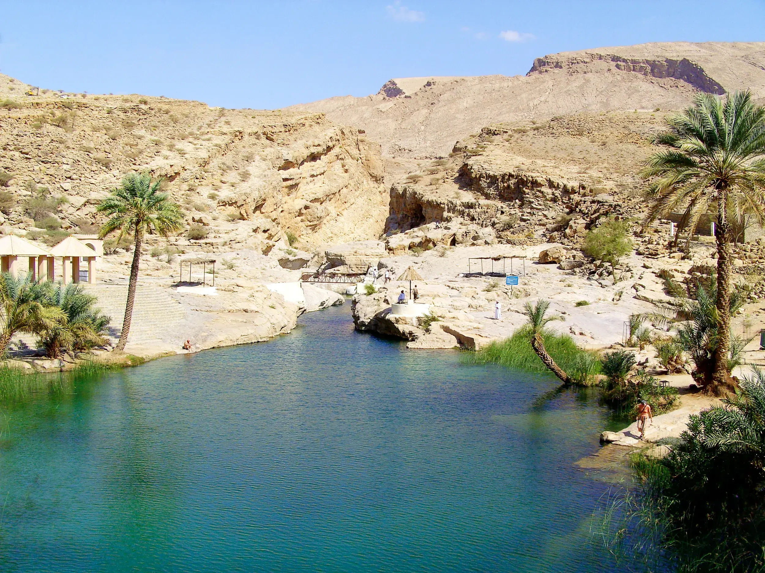 Wanderer erfrischen sich an den smaragdgrünen Pools im Wadi Shab, einer Oase in der trockenen Felslandschaft Omans.