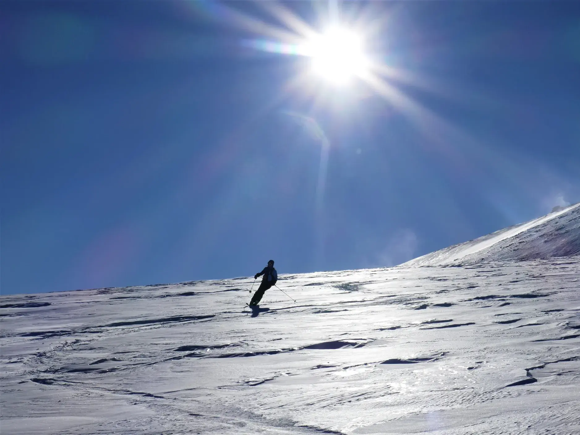 Ein Skitourengeher fährt bei strahlender Sonne einen weiten, unberührten Schneehang im Sharr-Gebirge im Kosovo hinab.