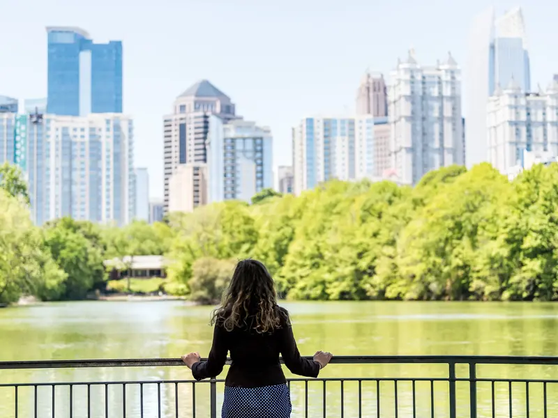 Teilnehmerin einer Studienreise blickt von einem Geländer über den See im Piedmont Park auf die sonnige Skyline von Atlanta.