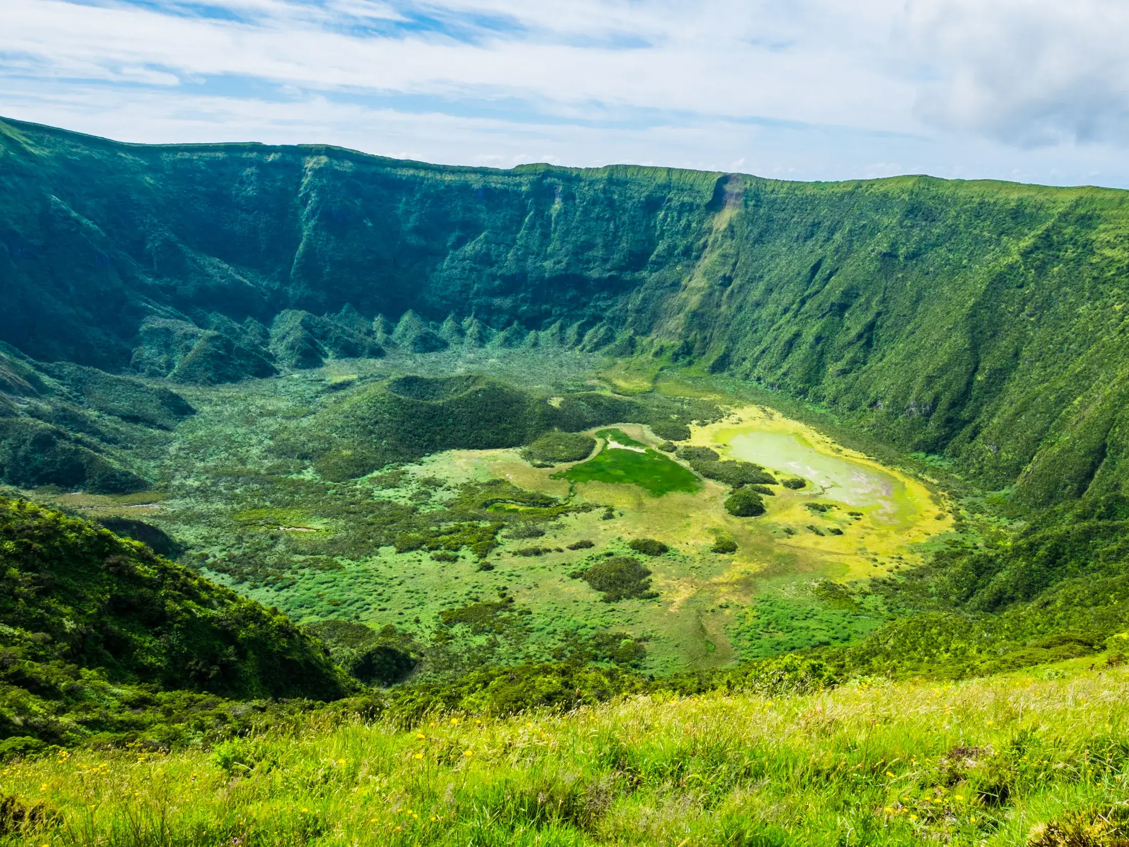 Wanderung auf den Azoren: Weitblick in die riesige, üppig grüne Caldeira auf der Insel Corvo mit ihrem kleinen See.