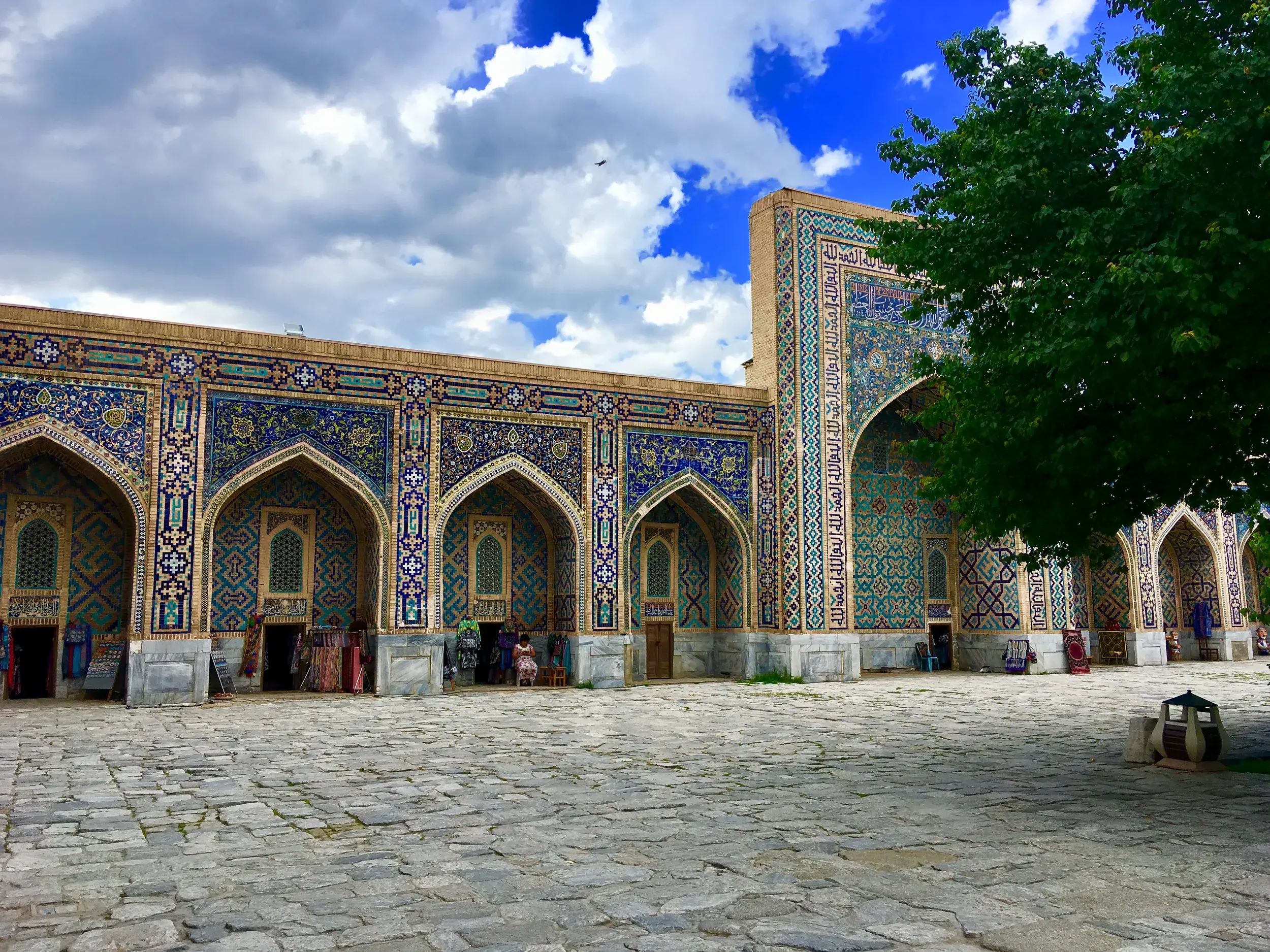 Gepflasterter Innenhof vor der prunkvollen Fassade der Tilla-Kori Medresse am Registan-Platz in Samarkand, Usbekistan.